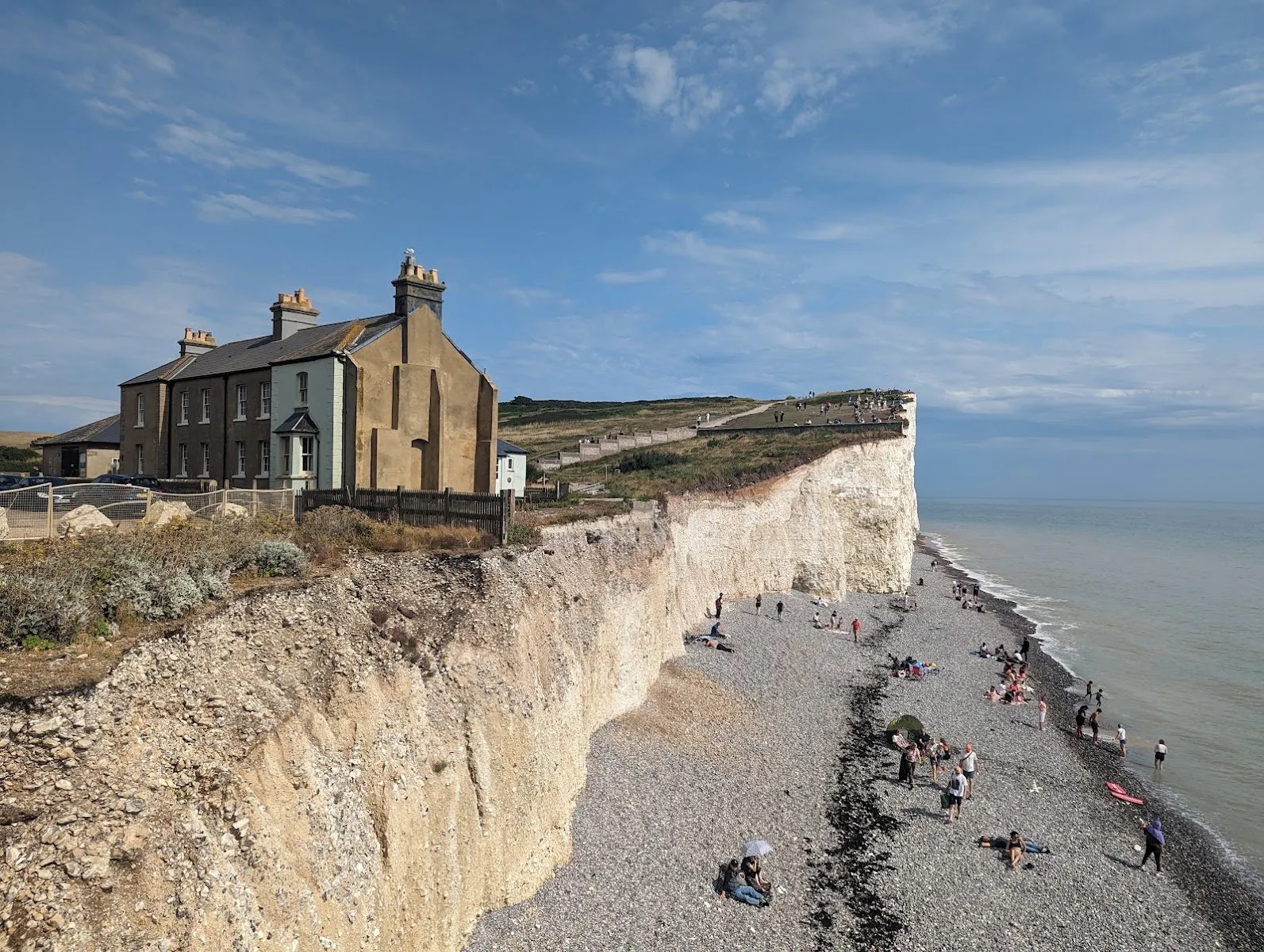 The coastguard cottages at Birling Gap on the clifftop, with the chalk cliffs and pebble beach below dotted with visitors