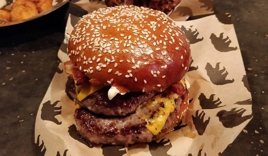 A burger with bacon and melted cheese in a sesame brioche bun, on paper printed with bear paw prints