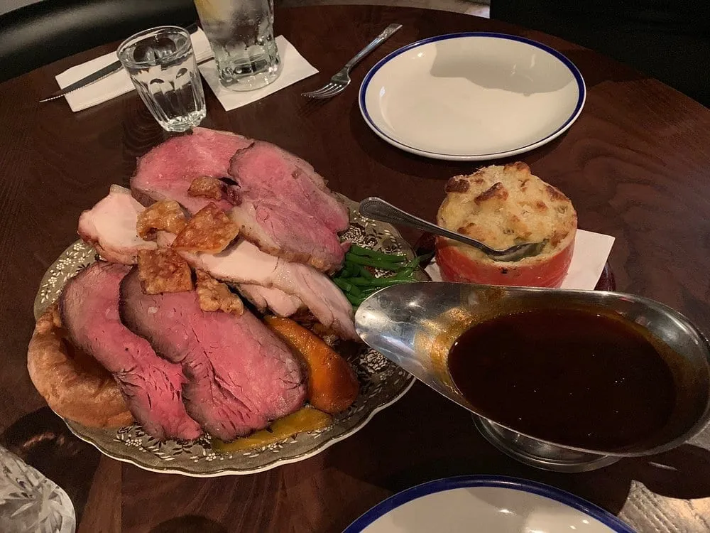 Blacklock's All In roast on a platter: slices of pink beef and pork with crackling, a Yorkshire pudding, roast carrots and green beans, with cauliflower cheese and a boat of gravy alongside
