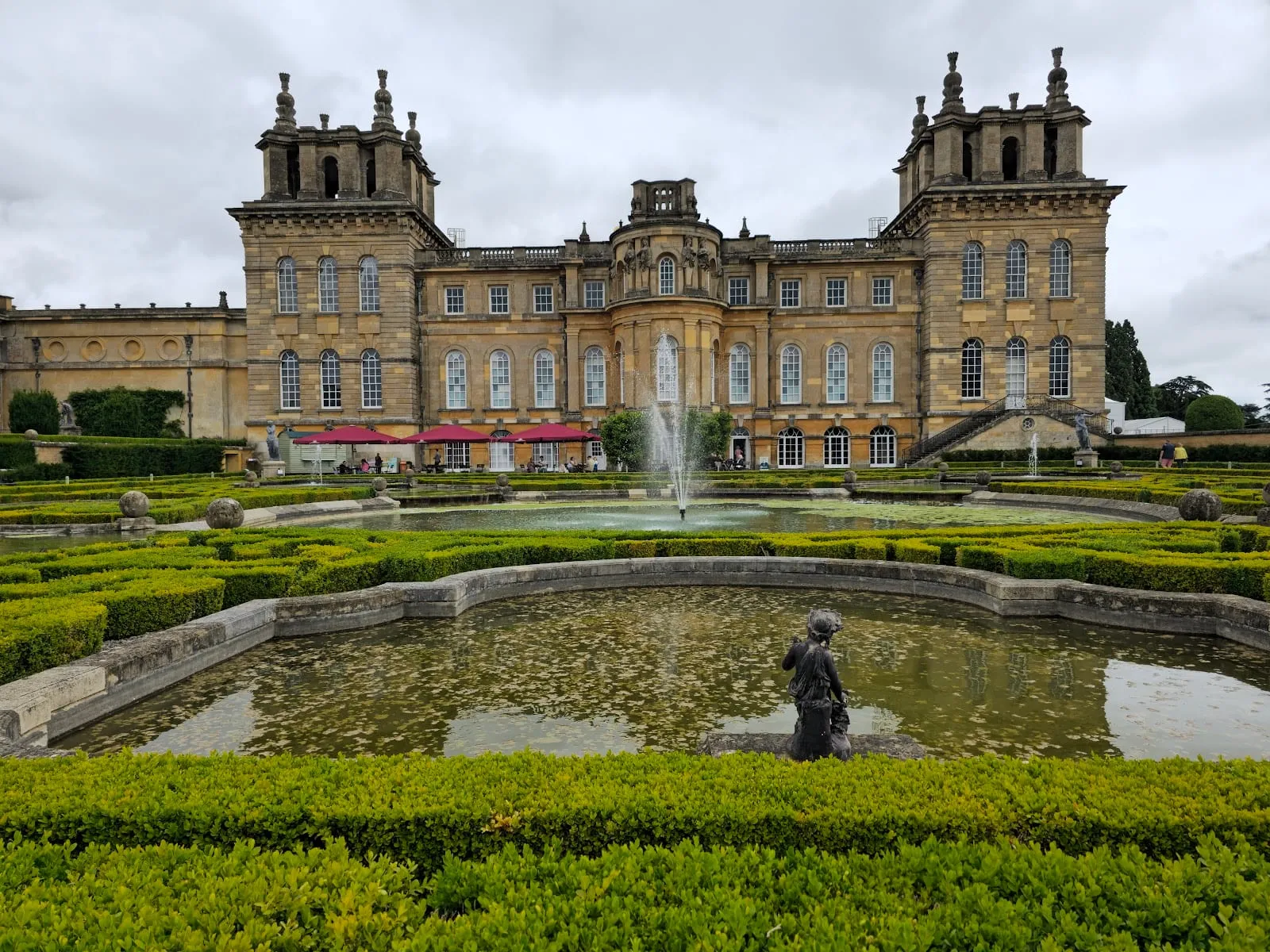 Blenheim Palace seen across its formal water garden, with clipped hedges and a fountain in front of the baroque facade