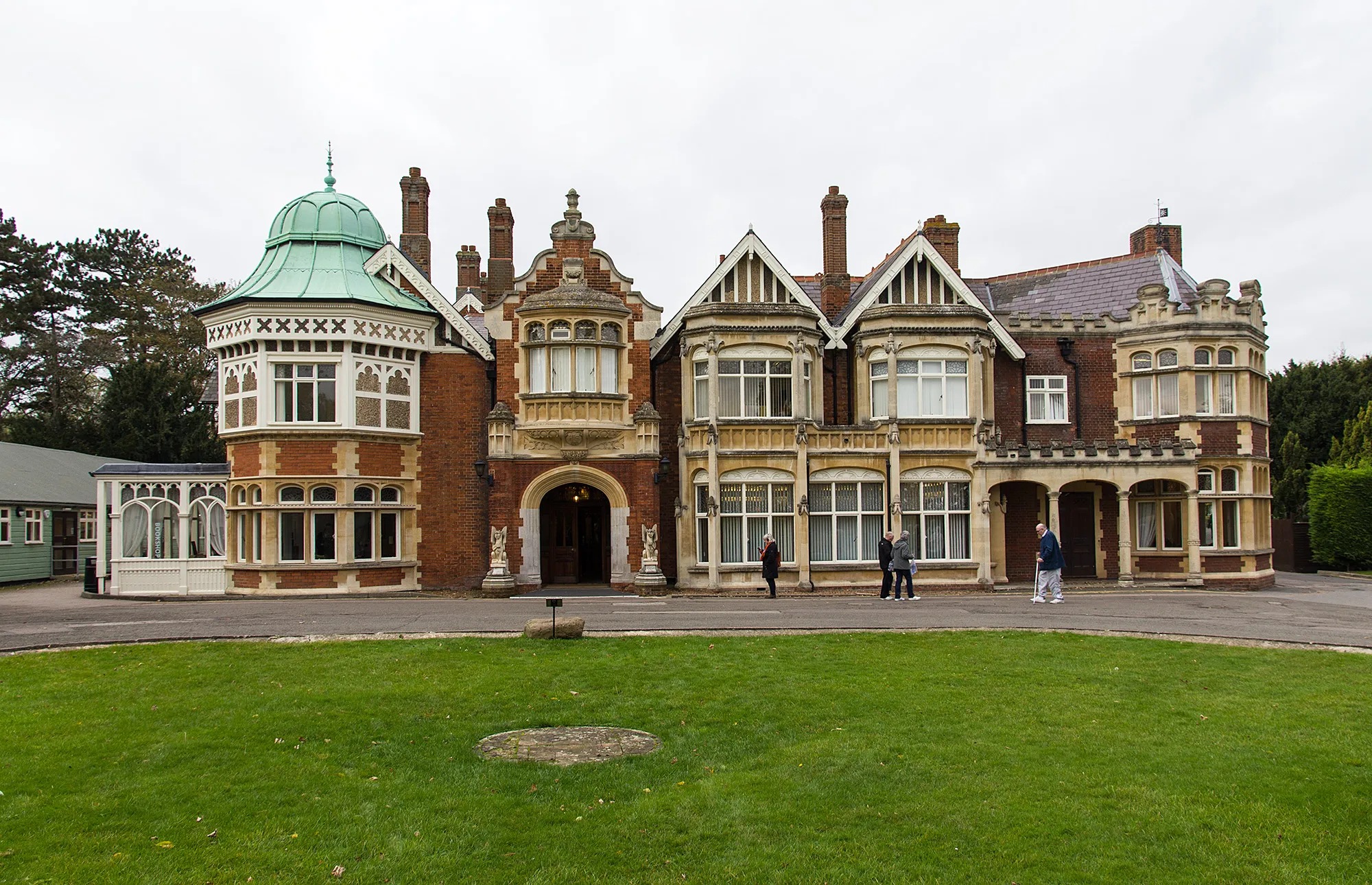 The Mansion at Bletchley Park, a Victorian house in red brick and pale stone with a green copper dome over one bay, visitors walking past the front door
