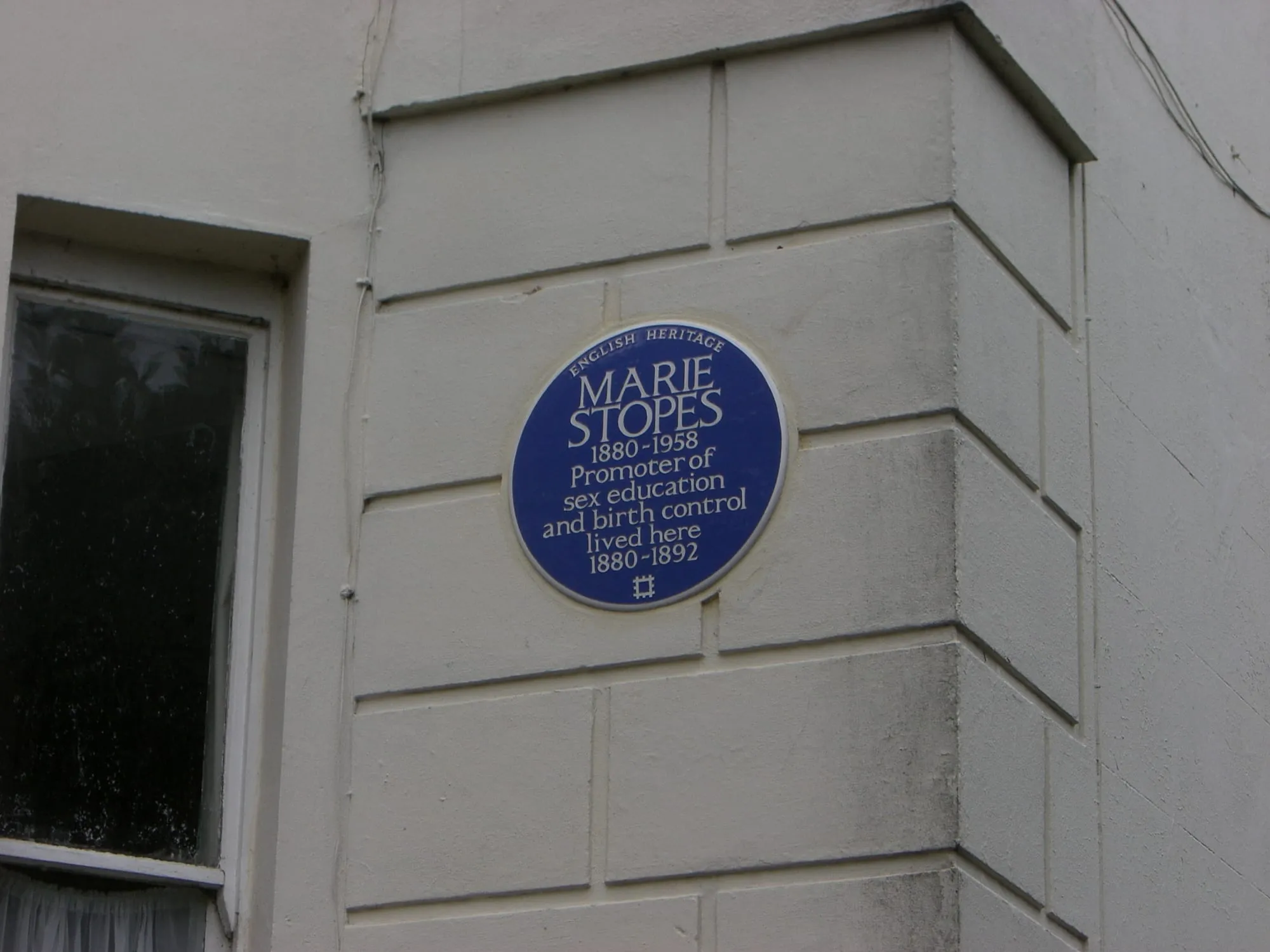 A round blue English Heritage plaque mounted on a London brick wall