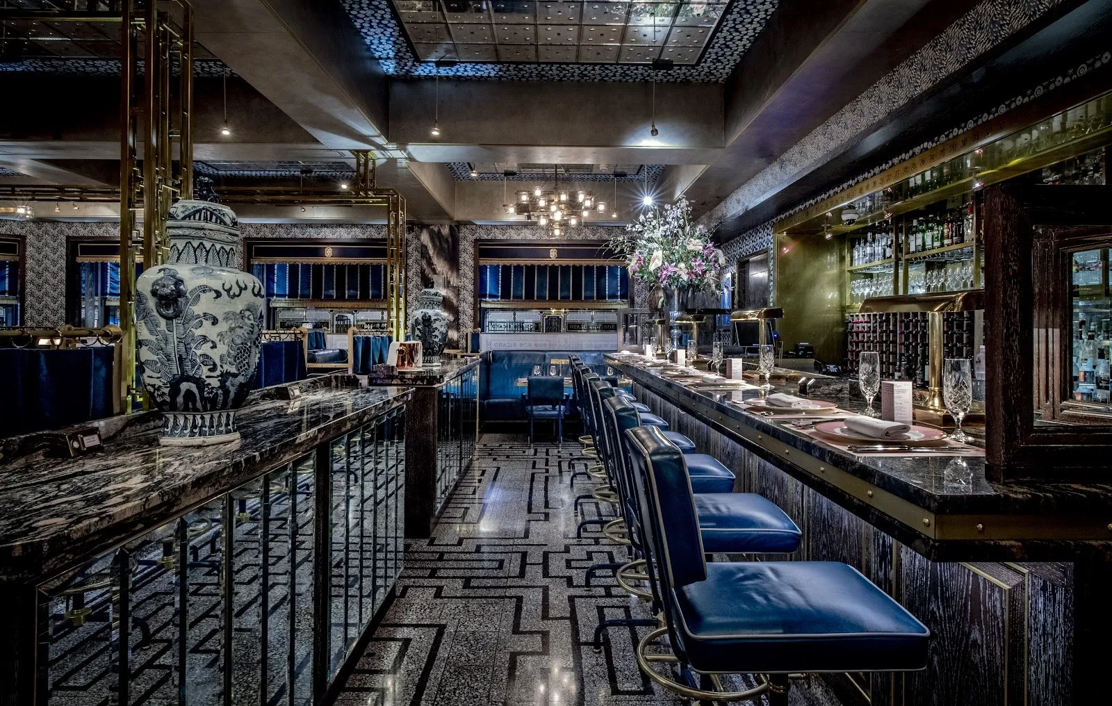 A dark art deco bar with navy leather stools and a patterned floor