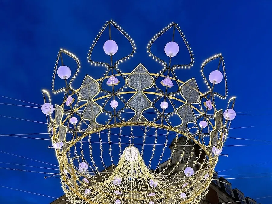 One of the Bond Street crowns against a deep blue evening sky, a ring of gold lights topped with heart-shaped points and lilac globes, with strands of light hanging inside it
