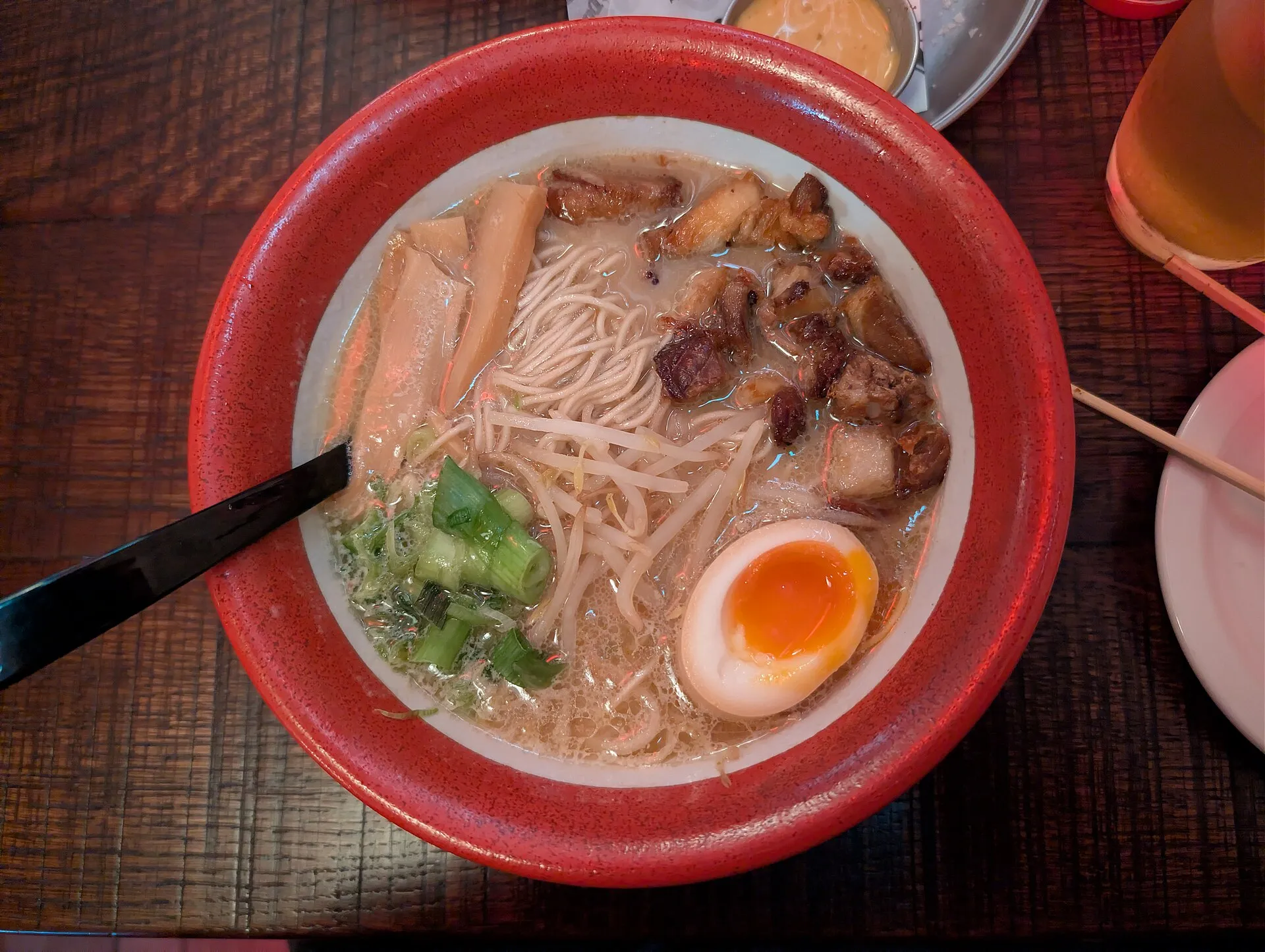A red-rimmed bowl of Yuzu Tonkotsu at Bone Daddies, seen from above, with fried pork belly, bamboo shoots, beansprouts, spring onion and a halved soy egg in pale pork broth
