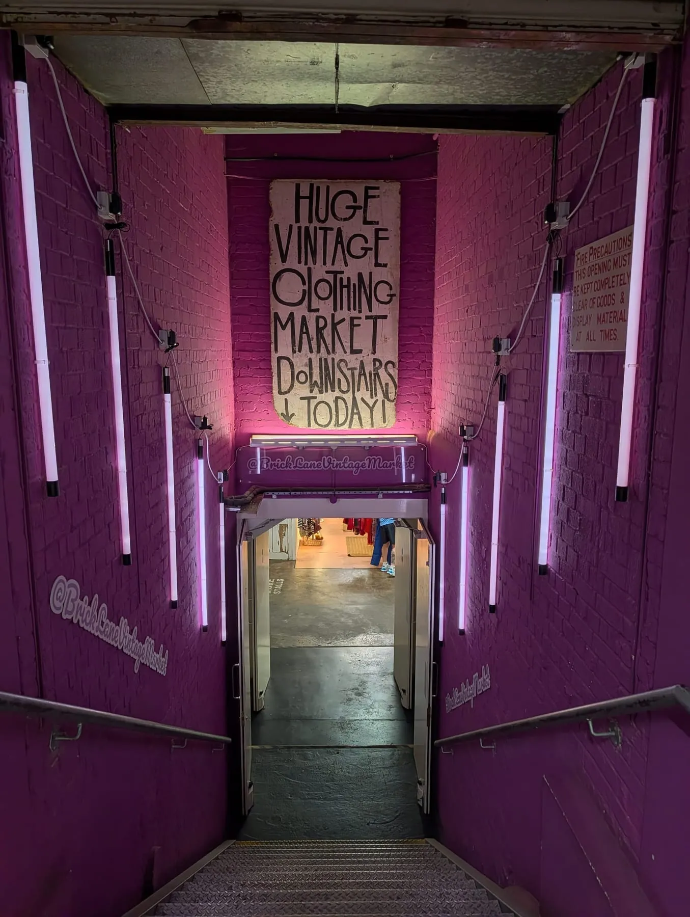 A pink-painted entrance lit by vertical neon tubes, signed Huge Vintage Clothing Market Downstairs, on Brick Lane