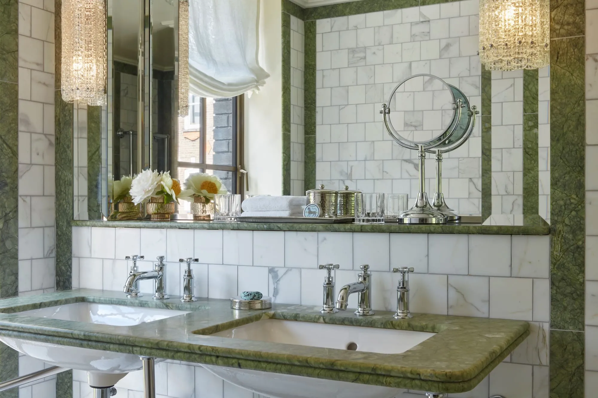 The bathroom at Broadwick Soho, with a green marble double vanity, white subway tile and traditional cross-head taps