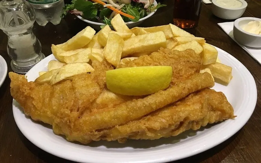 A large battered fillet and thick-cut chips on a white plate at Brockley's Rock, with a lemon wedge, a side salad and tartare sauce