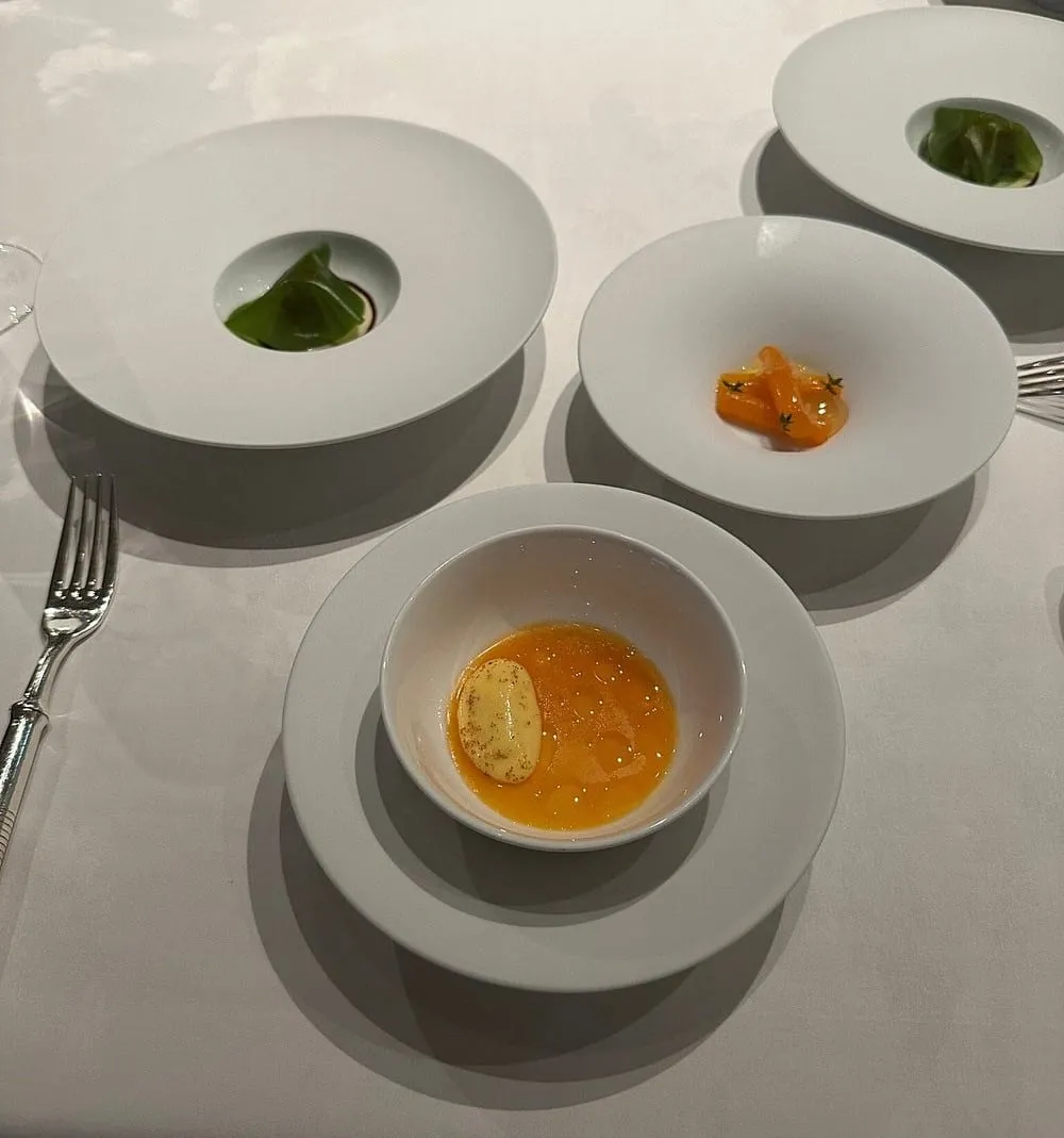 Four small tasting-menu courses on separate white plates and a bowl, each holding a single mouthful, on a white tablecloth