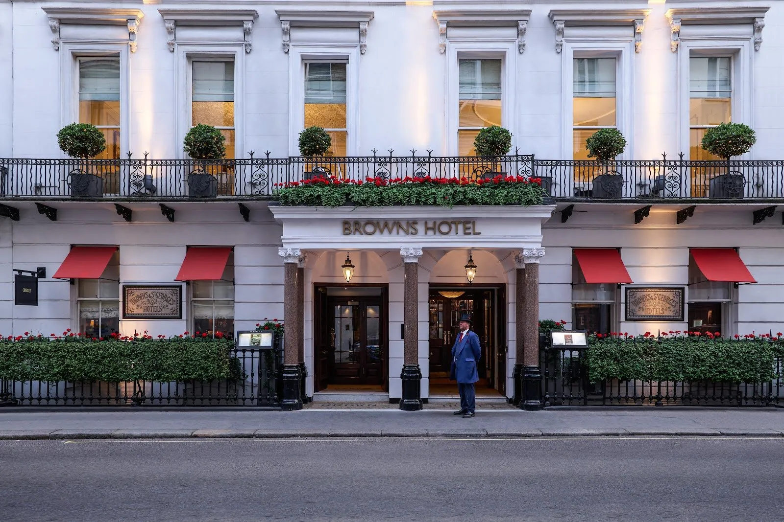 The Georgian facade of Brown's Hotel on Albemarle Street with red striped window awnings and a uniformed doorman