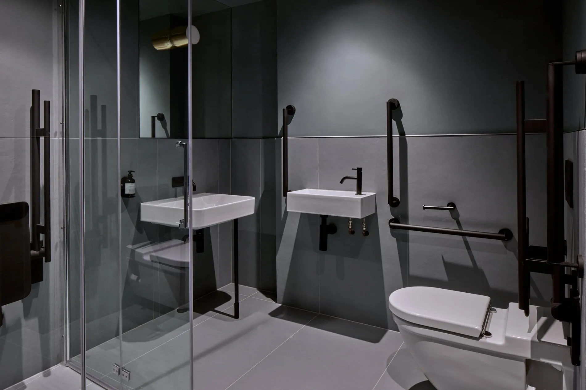 The bathroom at Buckle Street Studios, with dark tile, twin wall-mounted basins and grab rails