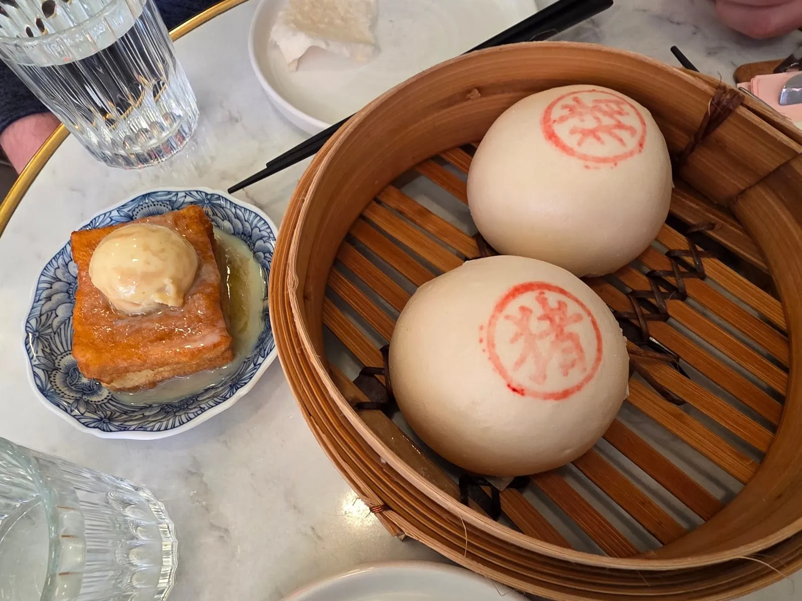 Two large steamed bao stamped with a red character, in a bamboo steamer
