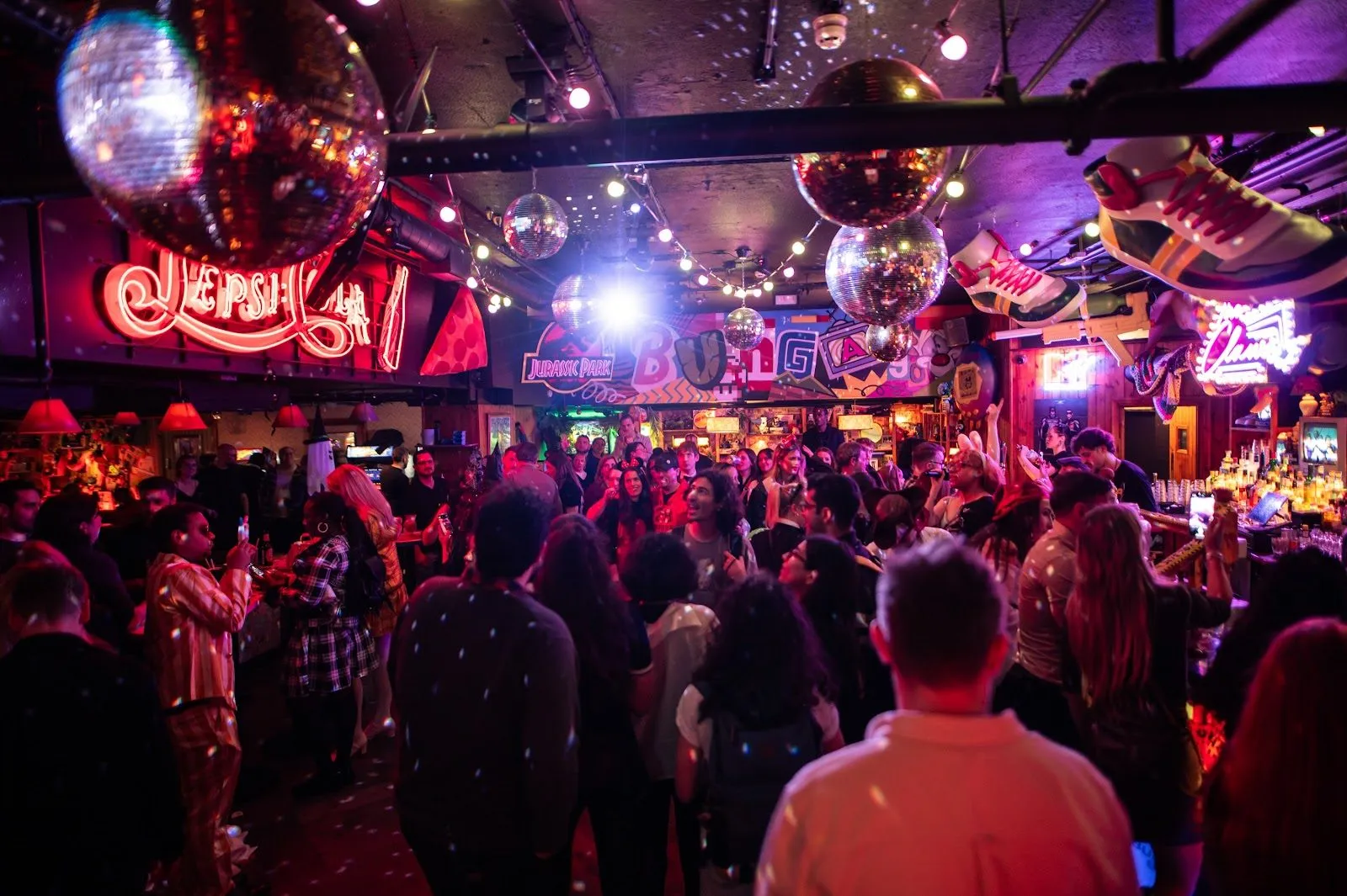 A crowd under disco balls and neon signs in the main bar at Bunga 90