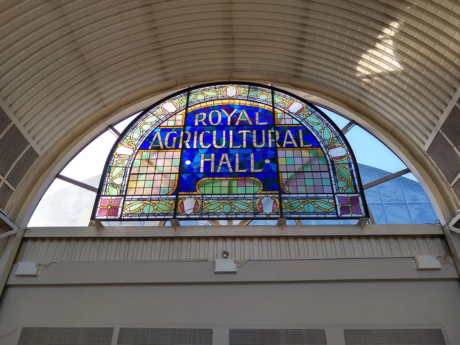 A stained-glass window reading "Royal Agricultural Hall" set into the barrel-vaulted roof of the Business Design Centre