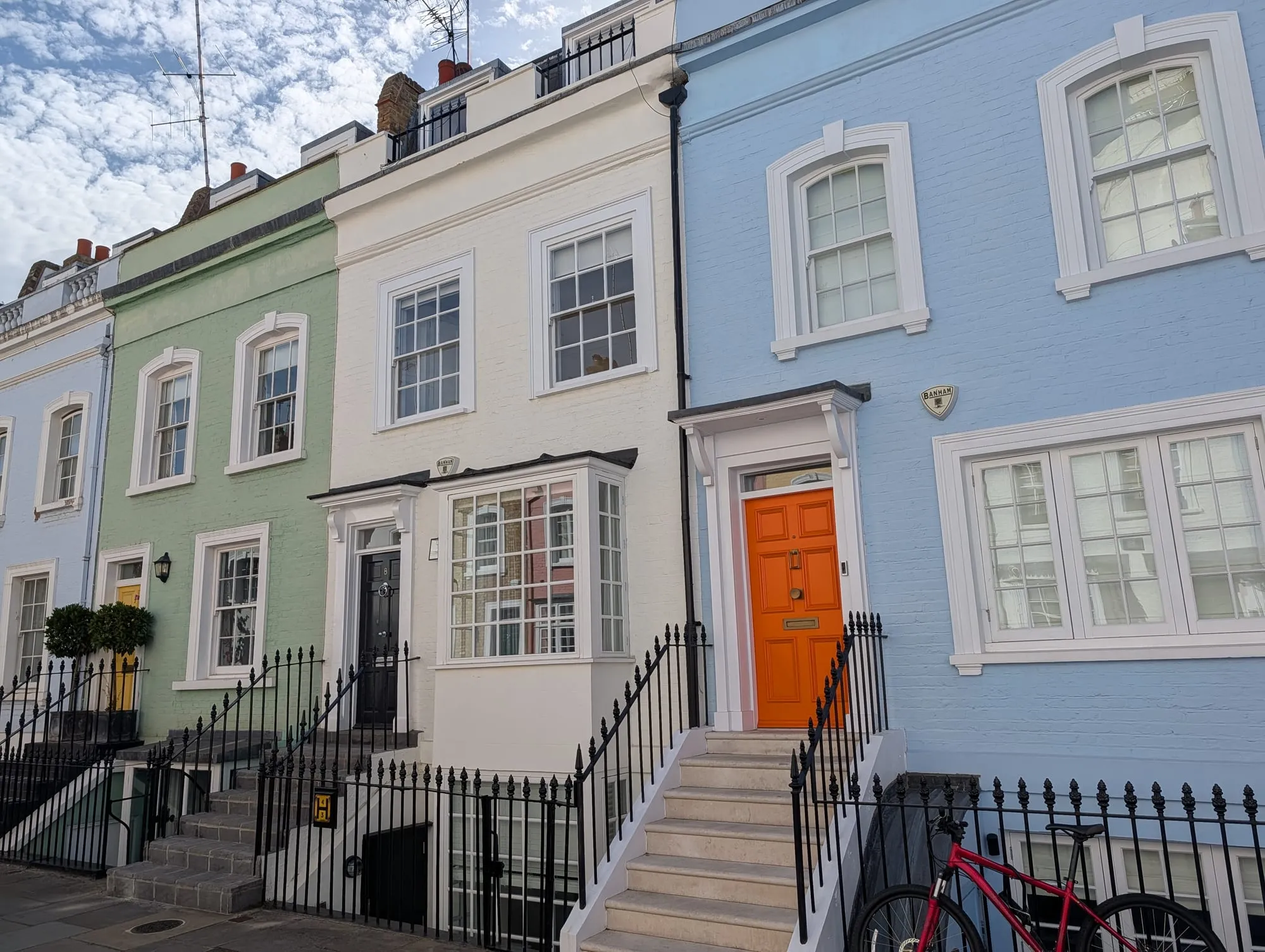 Two houses on Bywater Street, one sage green with an orange door and one pale blue