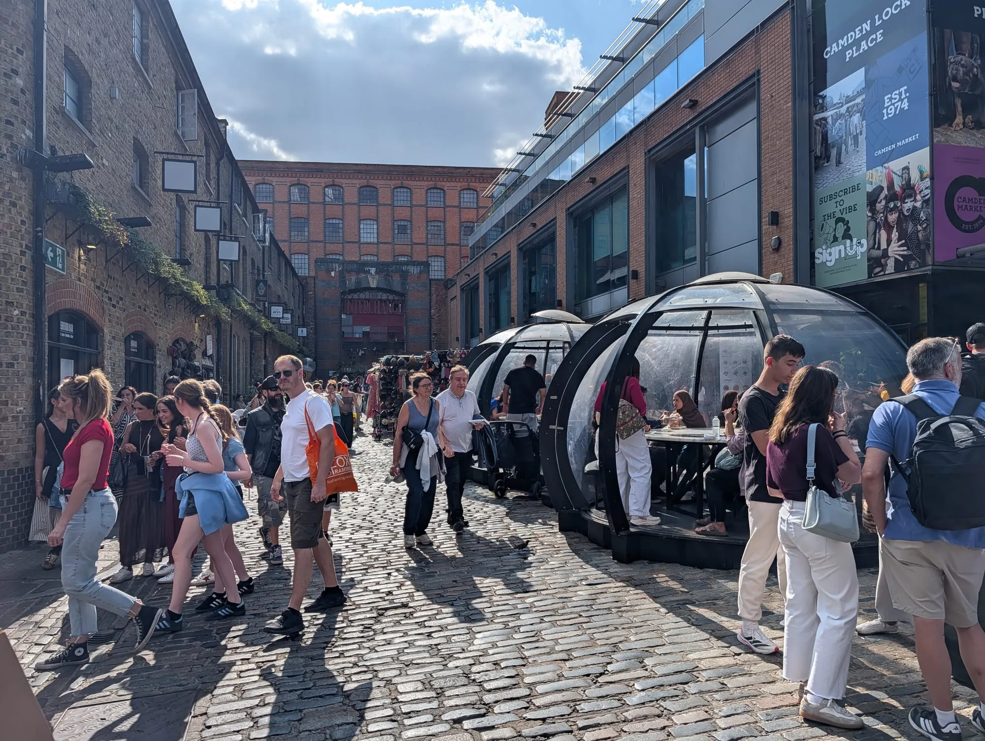 Crowds walking between glass-domed outdoor dining pods on the cobbles of Camden Lock Place