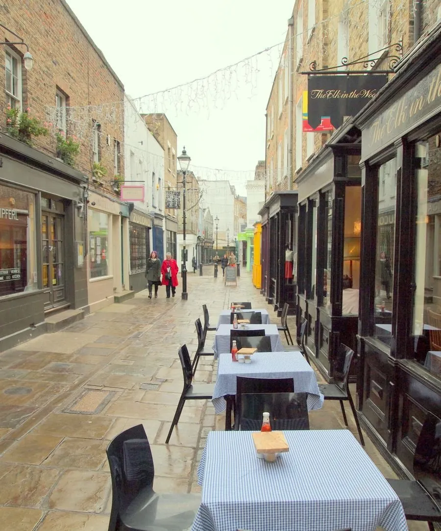 Antique dealers' shopfronts in Camden Passage, Islington, with pavement café tables and string lights strung overhead