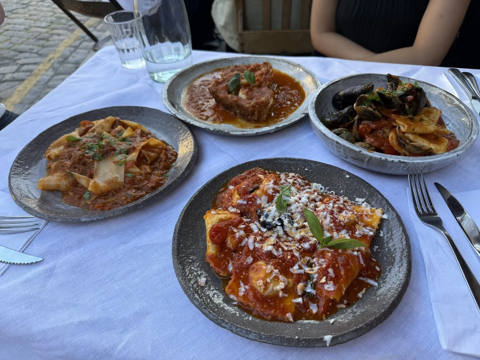 Four plates of pasta on a table, with cobbles at the edge of the frame