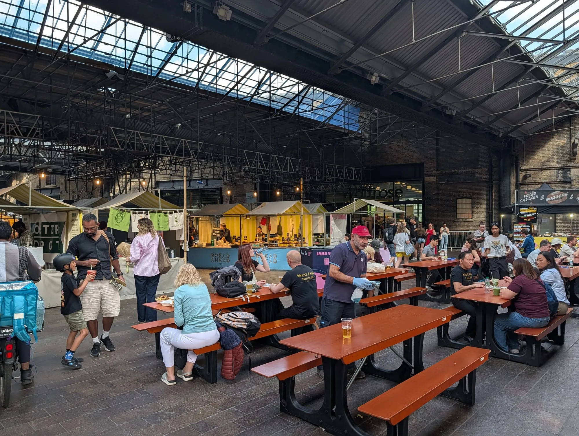 Traders and long picnic benches under the glass roof of Canopy Market in King's Cross
