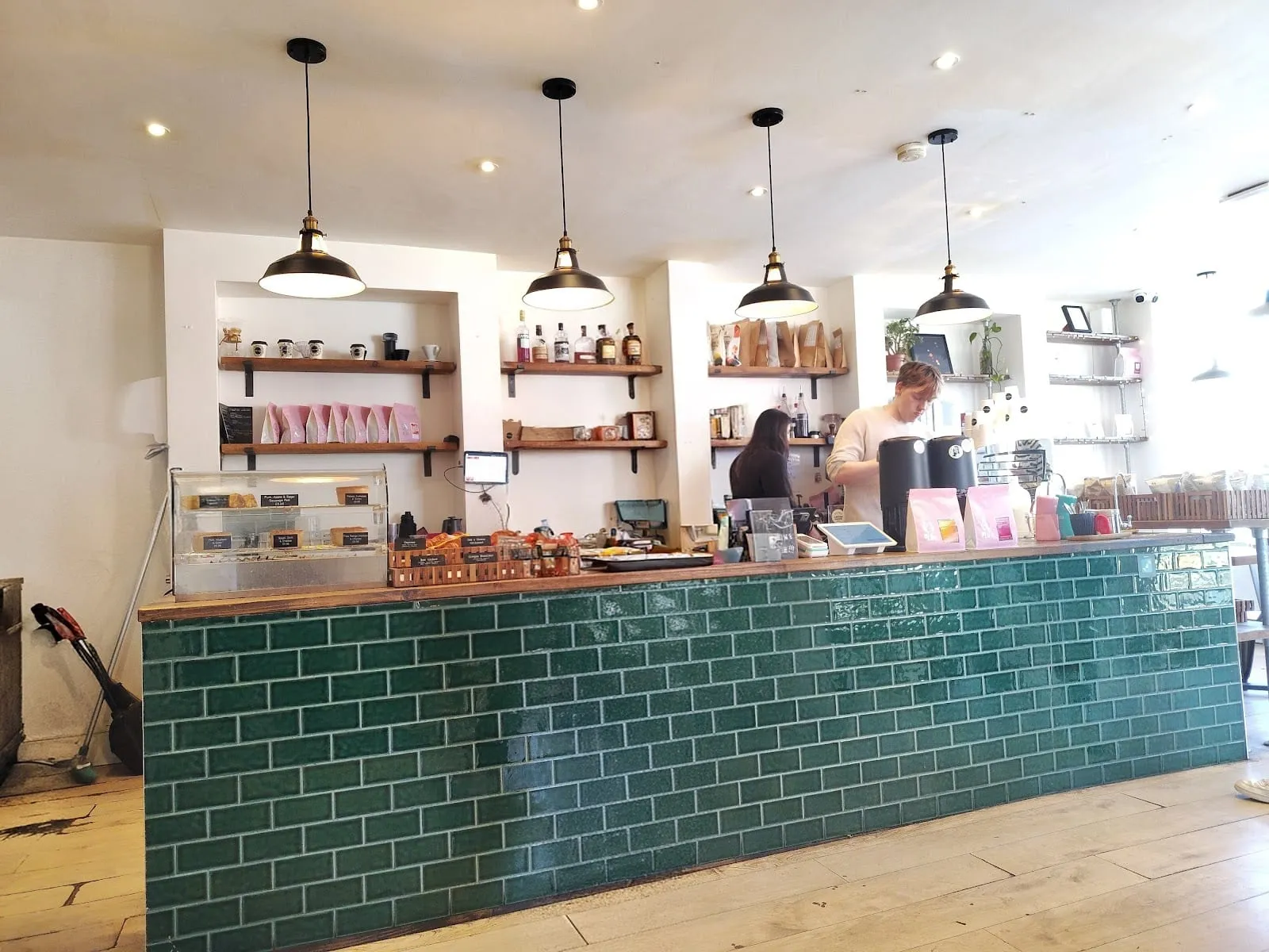 The green-tiled counter at Carbon Kopi, with pendant lights overhead and coffee bags on the shelves behind