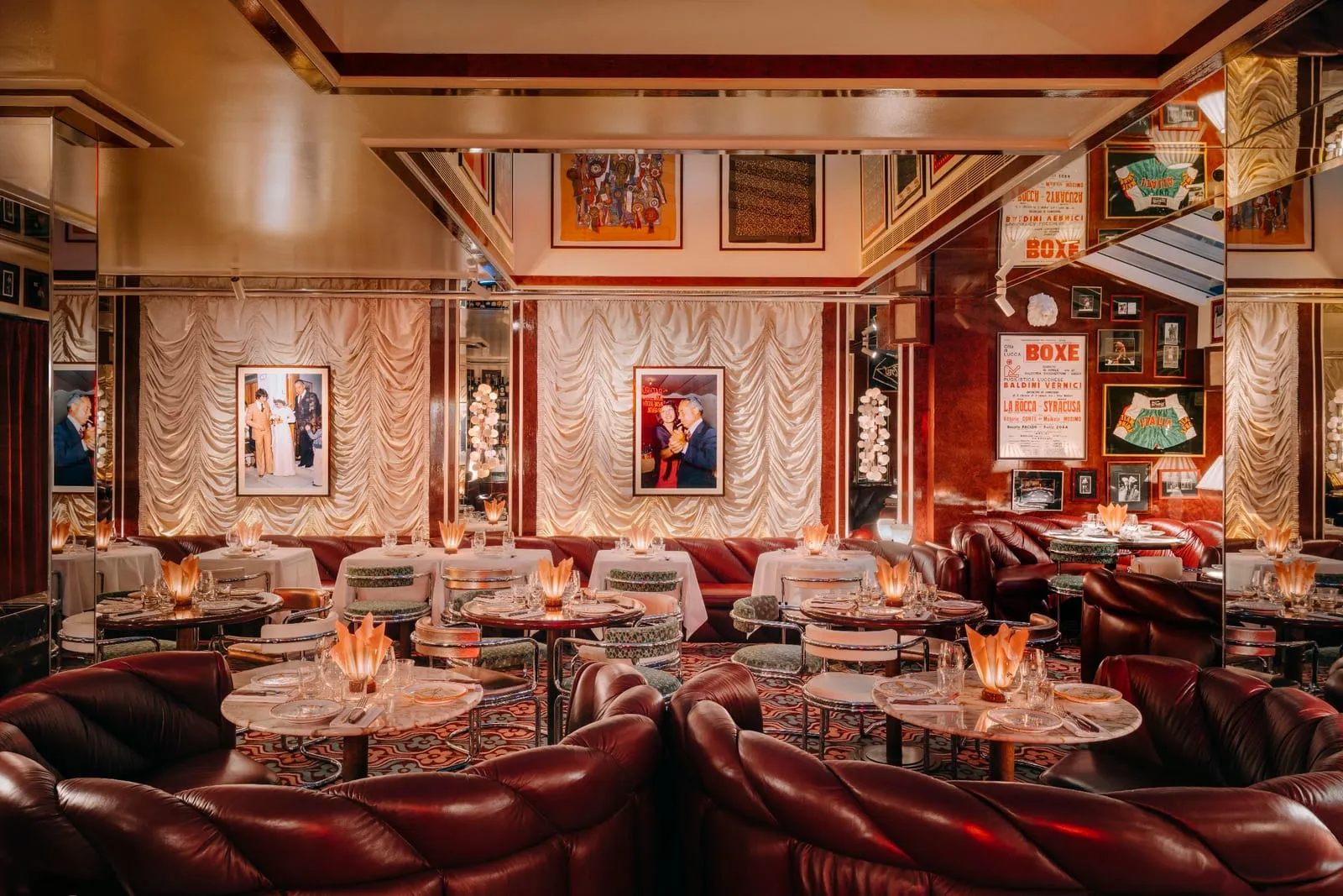 The dining room at Carlotta, deep red leather booths and small tables in front of ruched cream curtains, with framed boxing posters and photographs on the walls