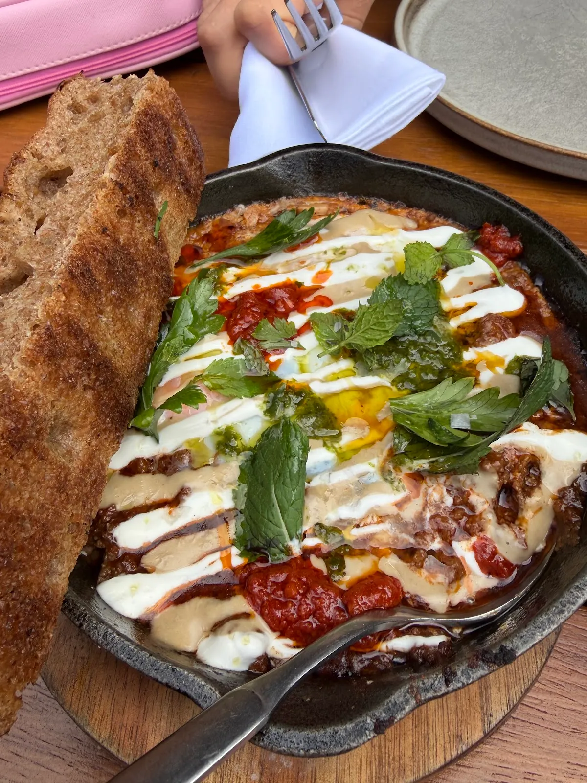 A baked egg dish in a cast iron pan with yoghurt, herbs and chilli, served with sourdough toast at Carmel