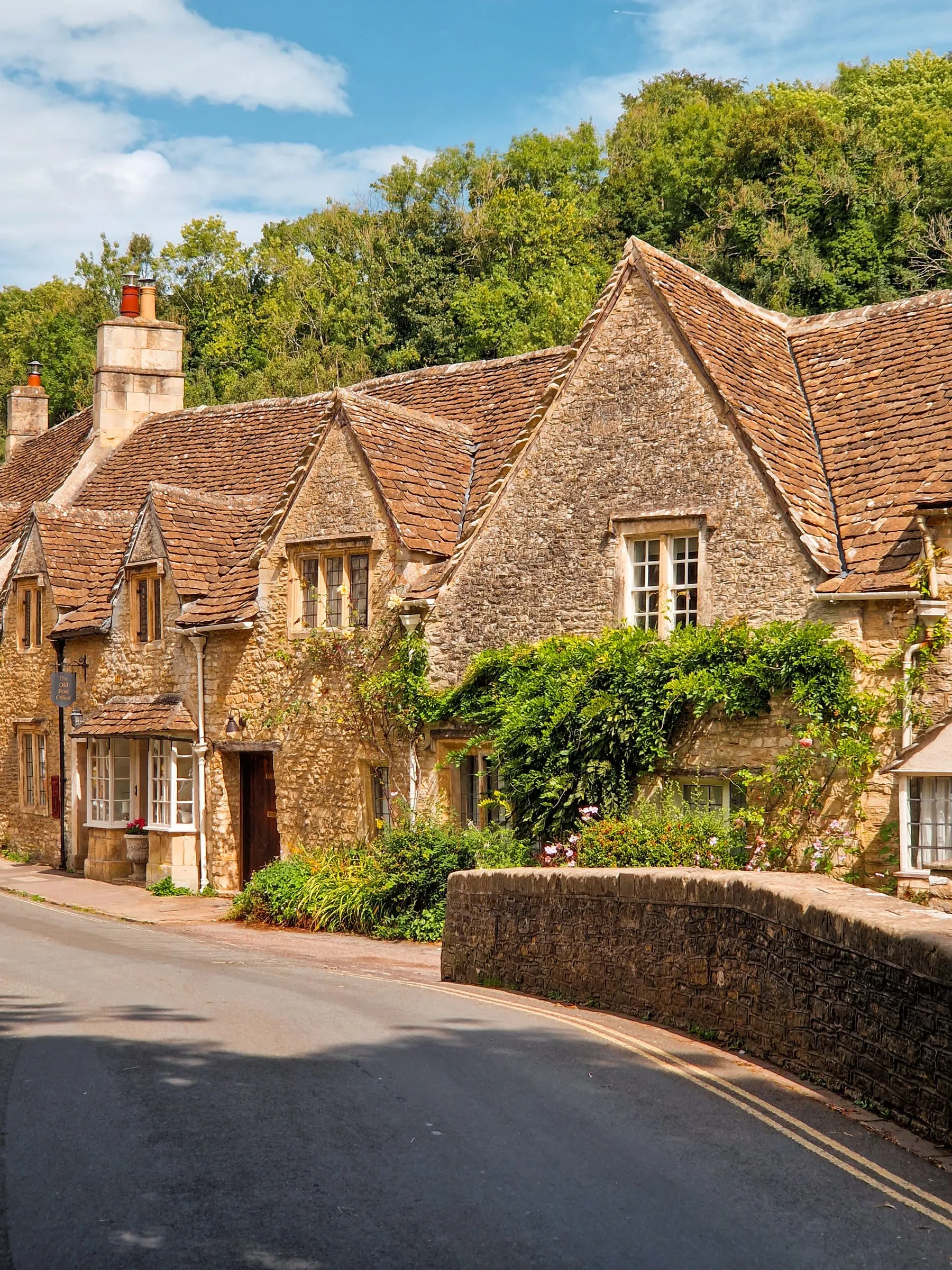 Stone cottages at Castle Combe, wisteria and flowers along their fronts, beside a low wall