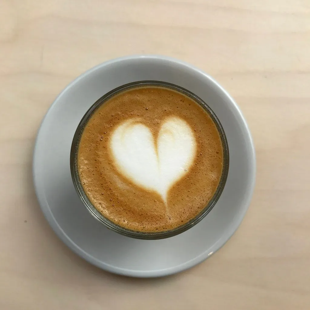 A flat white with heart latte art in a glass cup
