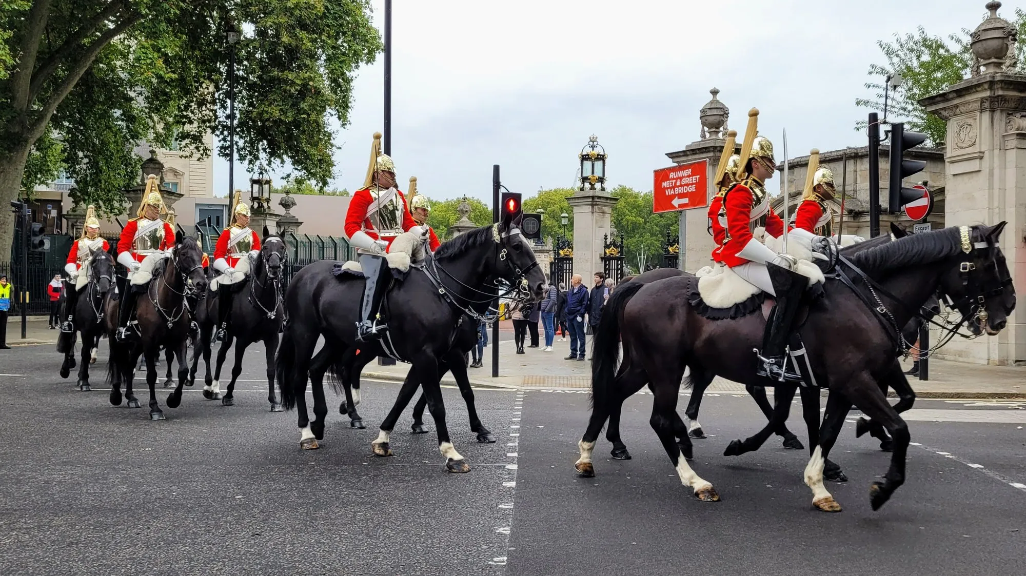 Mounted Household Cavalry troopers in red tunics and plumed helmets riding past Buckingham Palace's gates