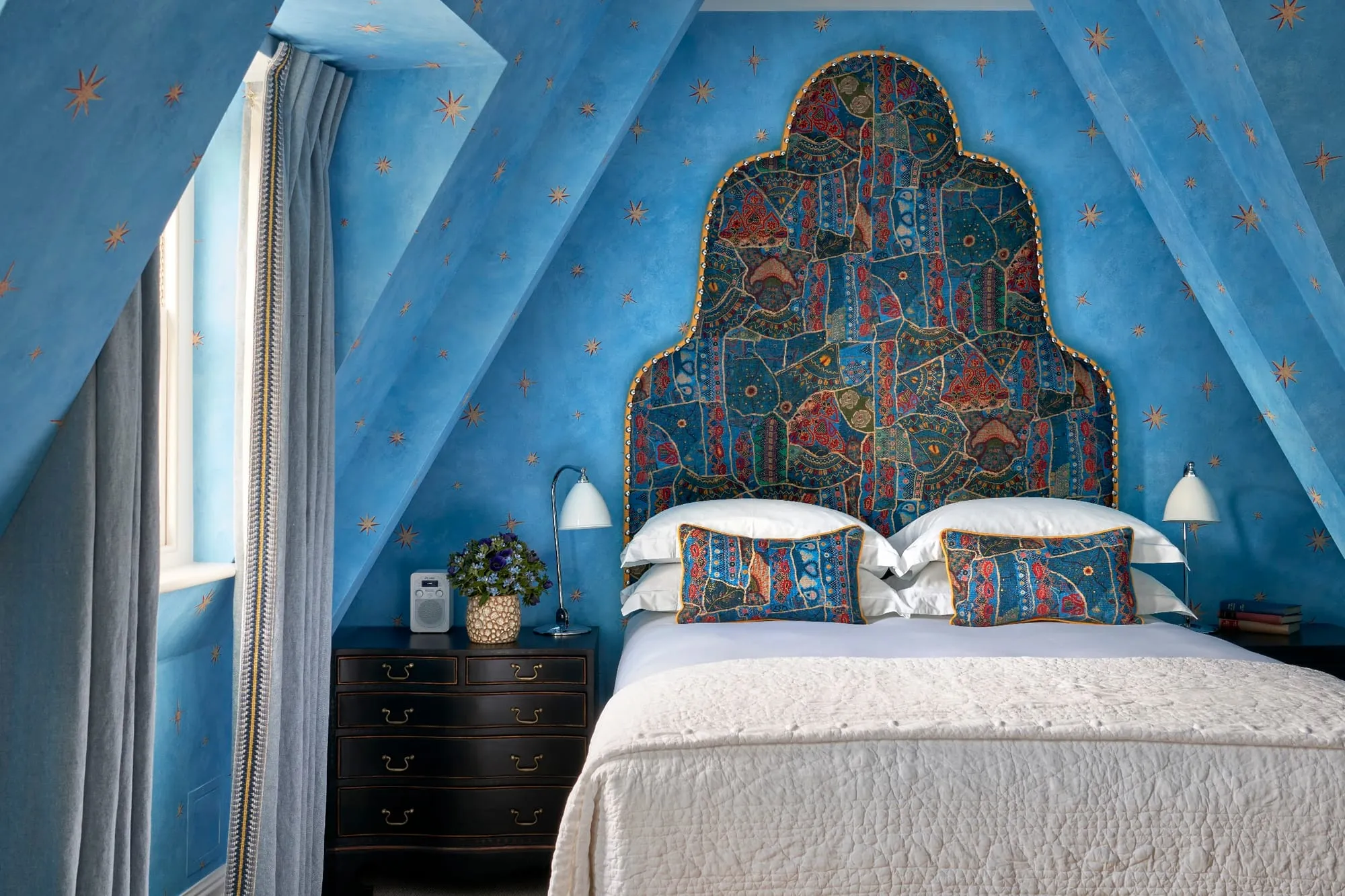 A Charlotte Street Hotel room with star-patterned blue walls and ceiling, and a richly patterned arched headboard