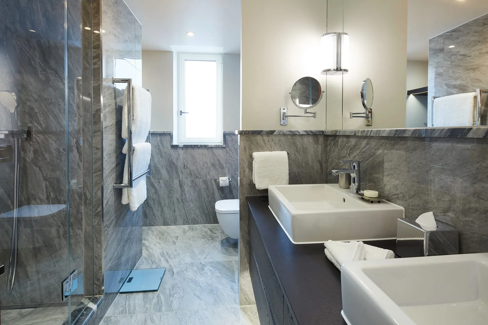 The bathroom at Cheval Gloucester Park, with grey marble tile, a walk-in shower and a double vanity with fold-out shaving mirrors