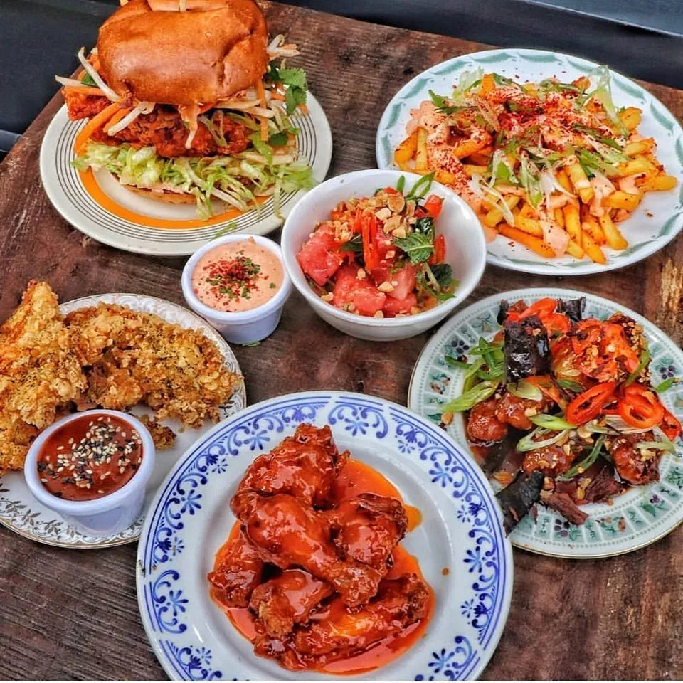 A spread of Chick'N'Sours dishes on a wooden board - a fried chicken sandwich, hot-sauced wings, seasoned fries, watermelon salad and dipping sauces