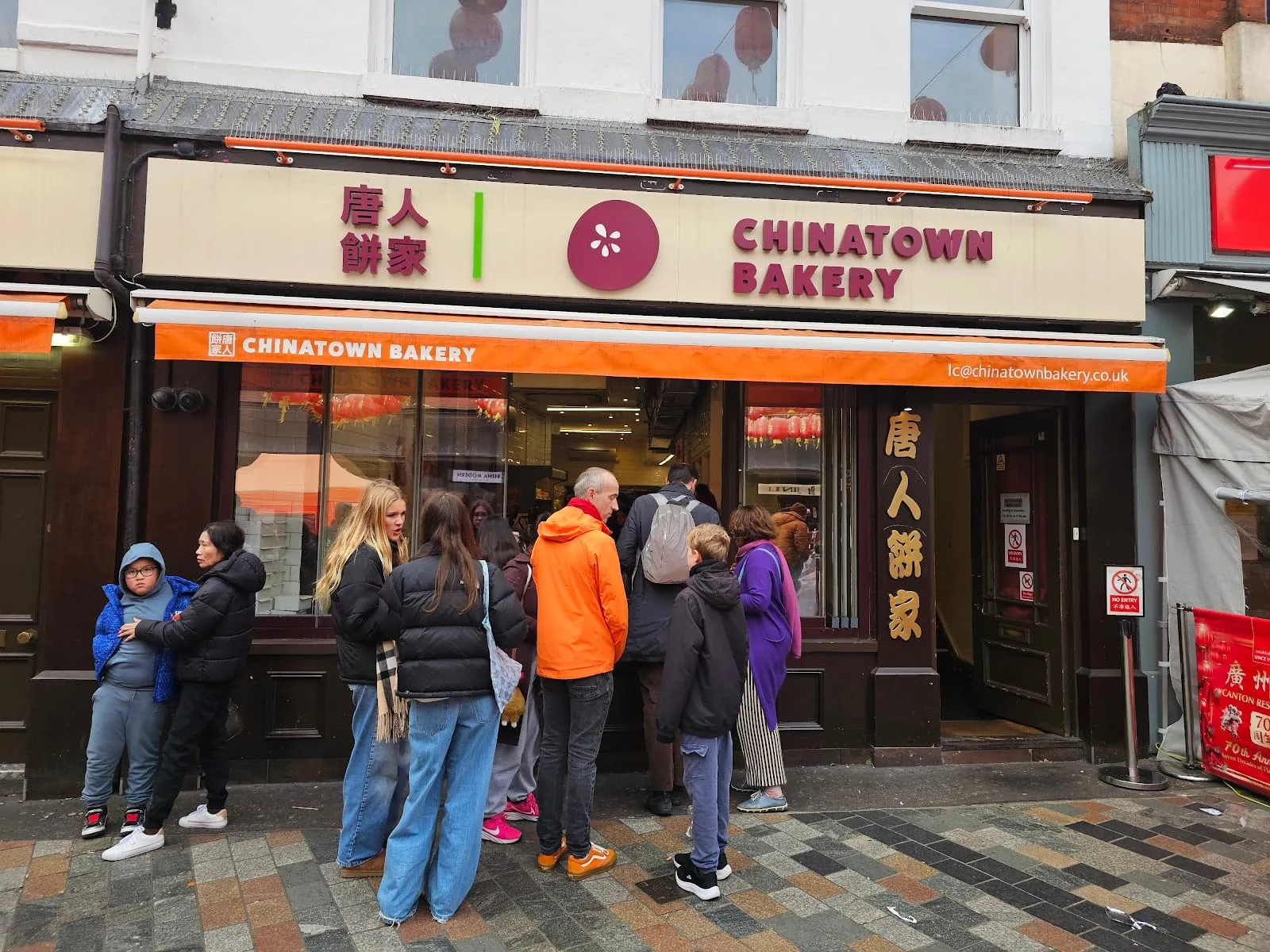 A queue of customers outside Chinatown Bakery's brown and orange shopfront on Newport Place
