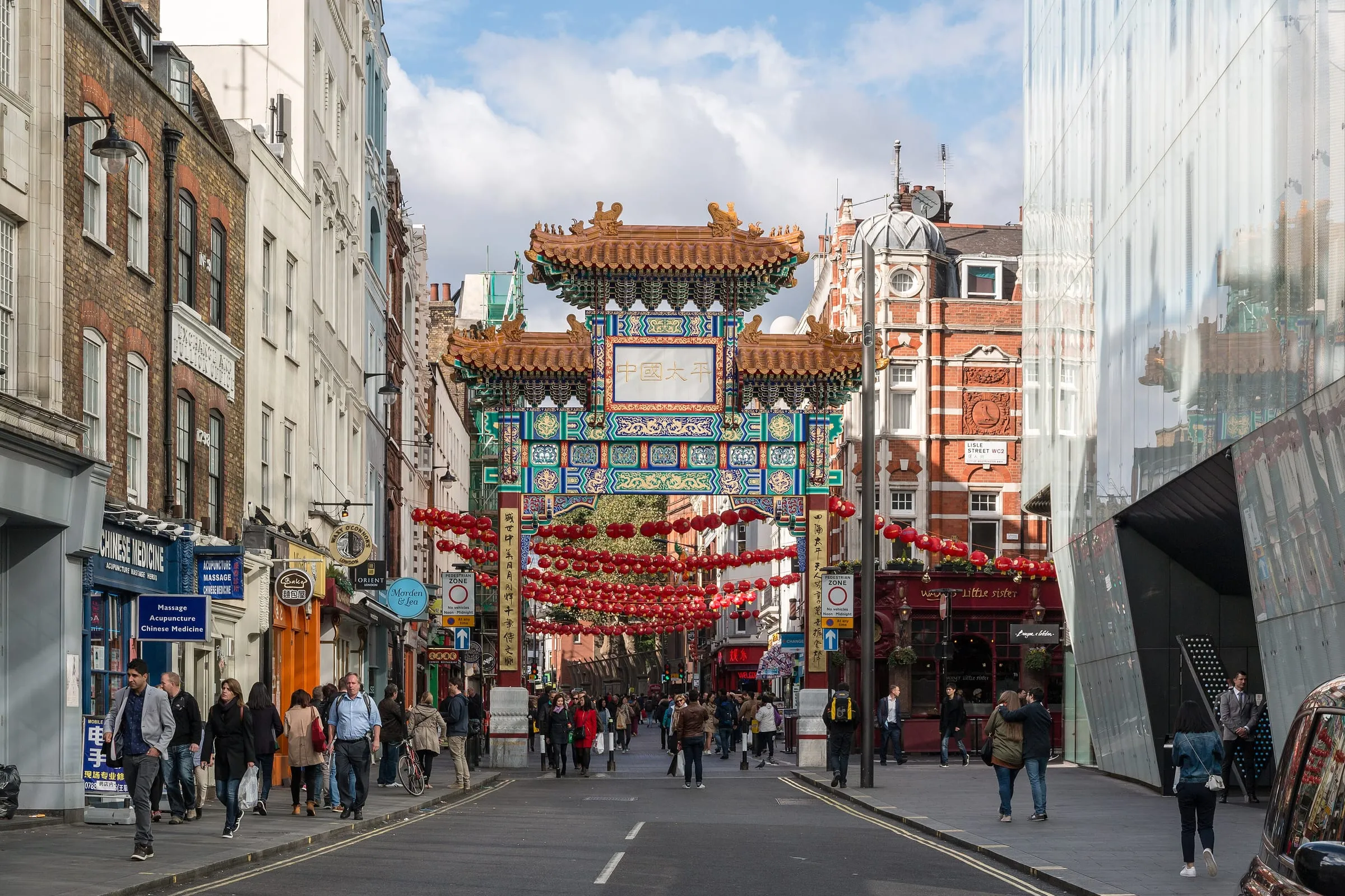 The Chinatown gate on Wardour Street, a painted Qing-style arch with tiled roofs, above a street strung with red lanterns
