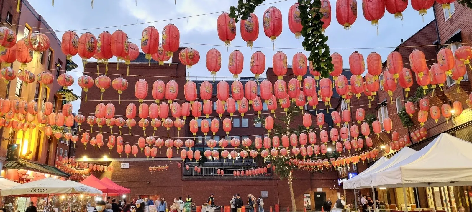Rows of red paper lanterns strung across Newport Place in Chinatown, with market-stall canopies below and the Newport Place WC2 street sign on the brick wall behind