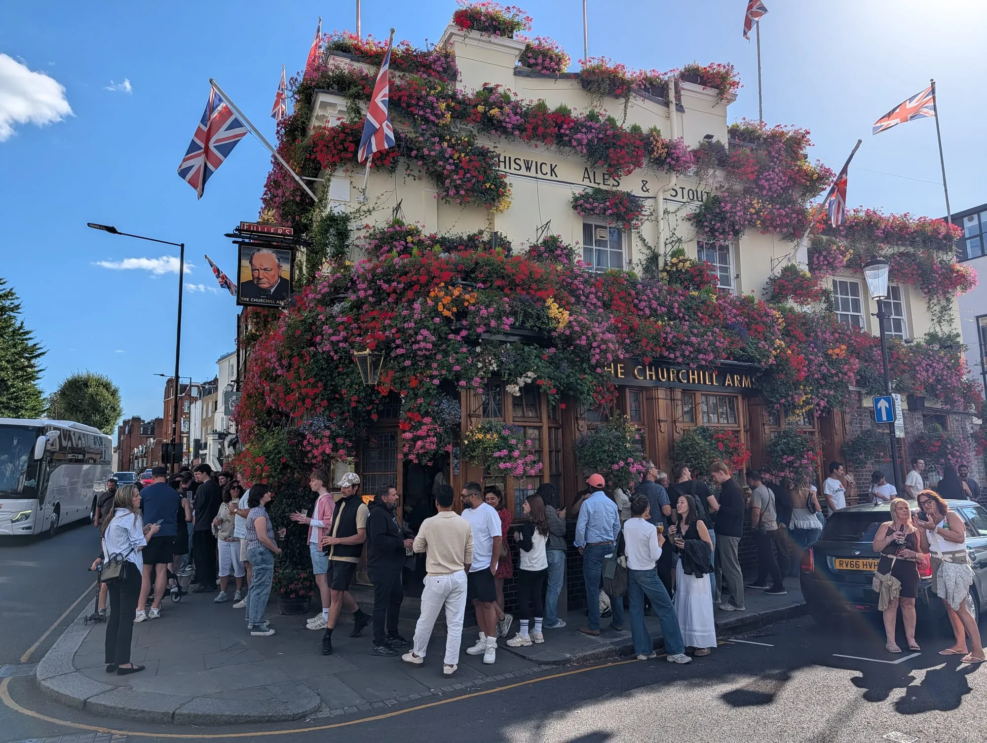 The Churchill Arms on Kensington Church Street, its whole frontage covered in hanging flower baskets and Union flags, with a crowd drinking outside