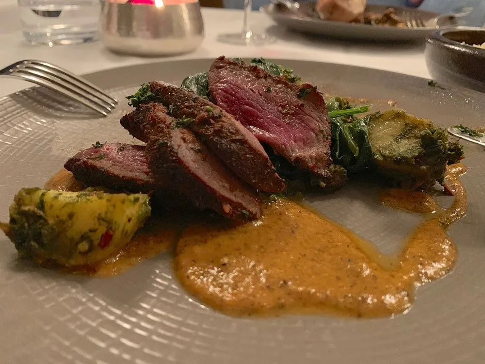 A plate at The Cinnamon Club: slices of spiced meat cooked pink, fanned over wilted greens with a spiced sauce pooled beside them