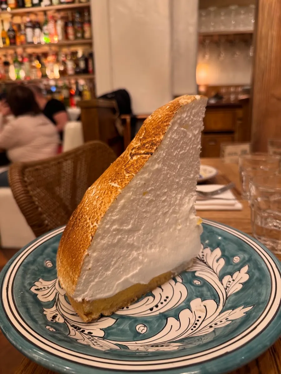 A tall slice of lemon meringue pie with a torched top, on a blue and white patterned plate