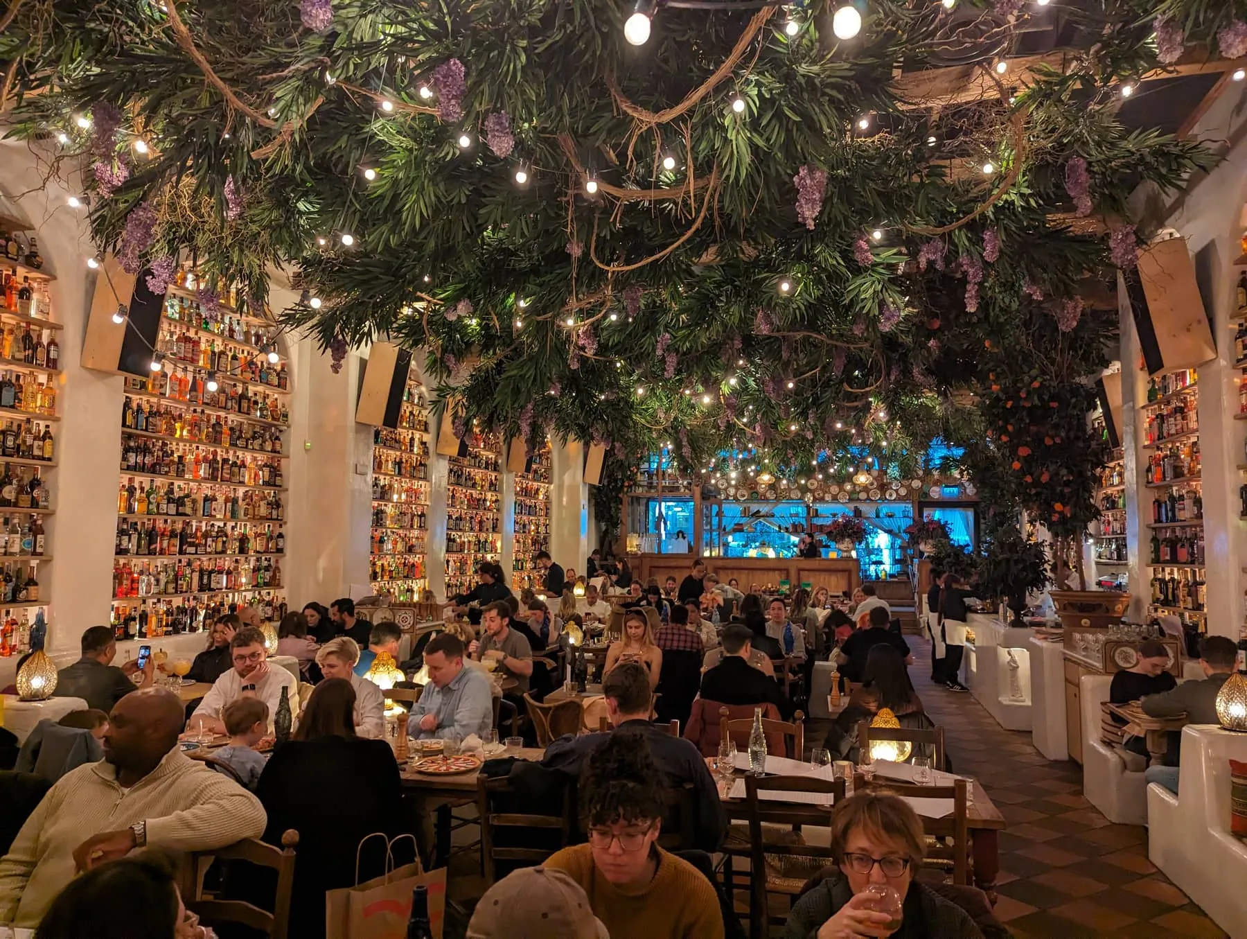 The dining room at Circolo Popolare, its walls stacked with thousands of bottles under a ceiling of hanging greenery and fairy lights