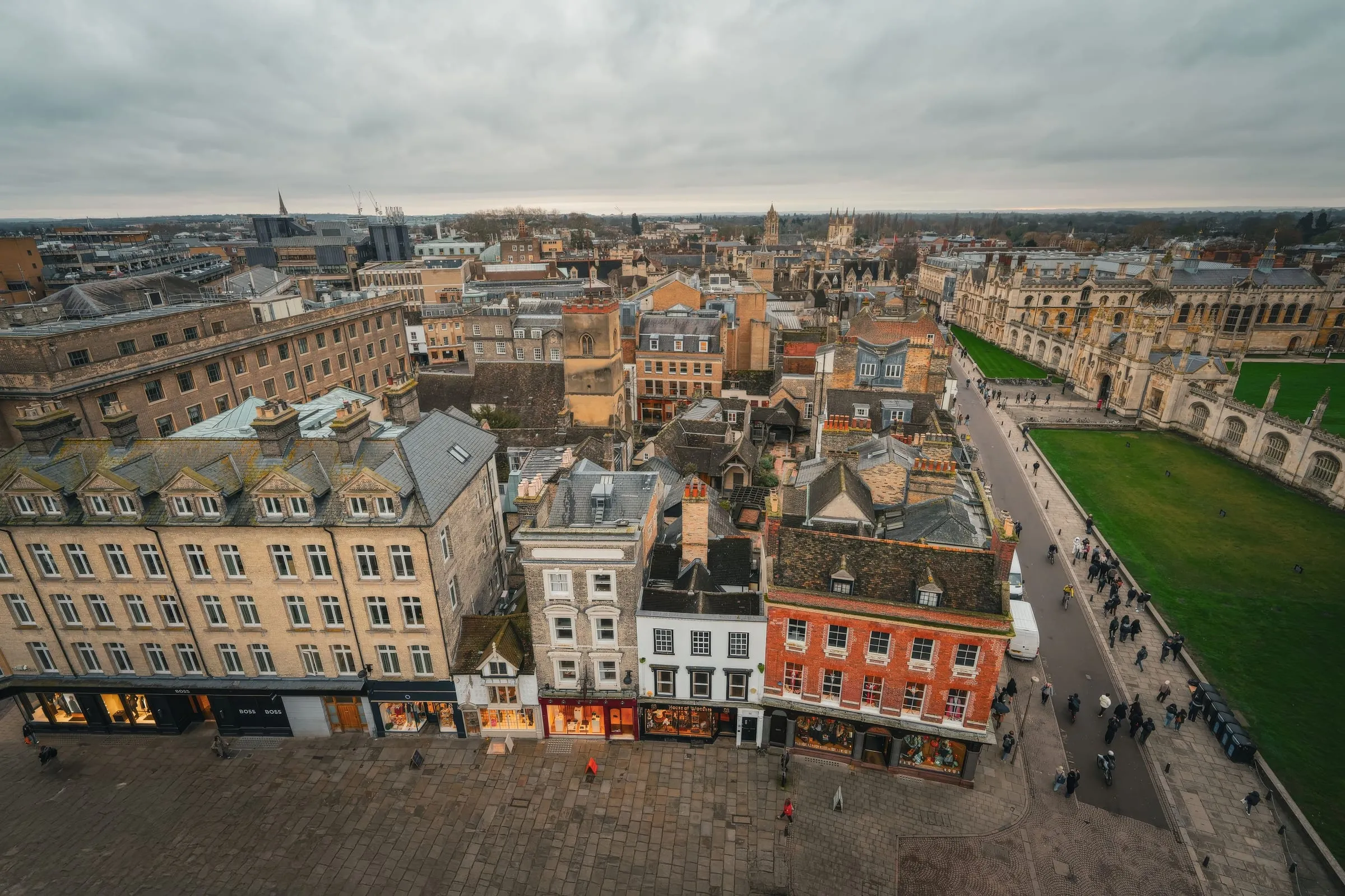 Cambridge rooftops from above, the market square and shopfronts below with college lawns beyond