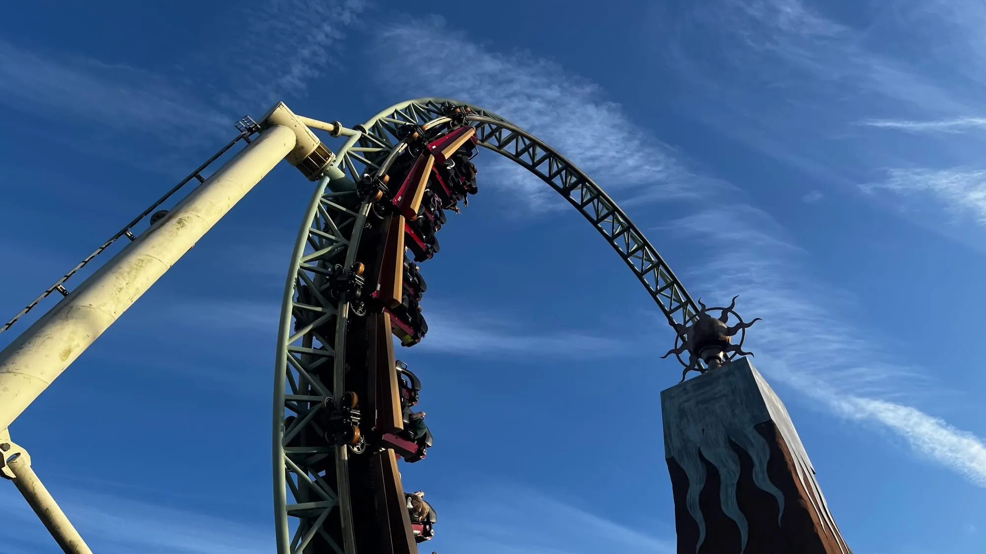 A Colossus train full of riders upside down at the top of the vertical loop at Thorpe Park, under a blue sky