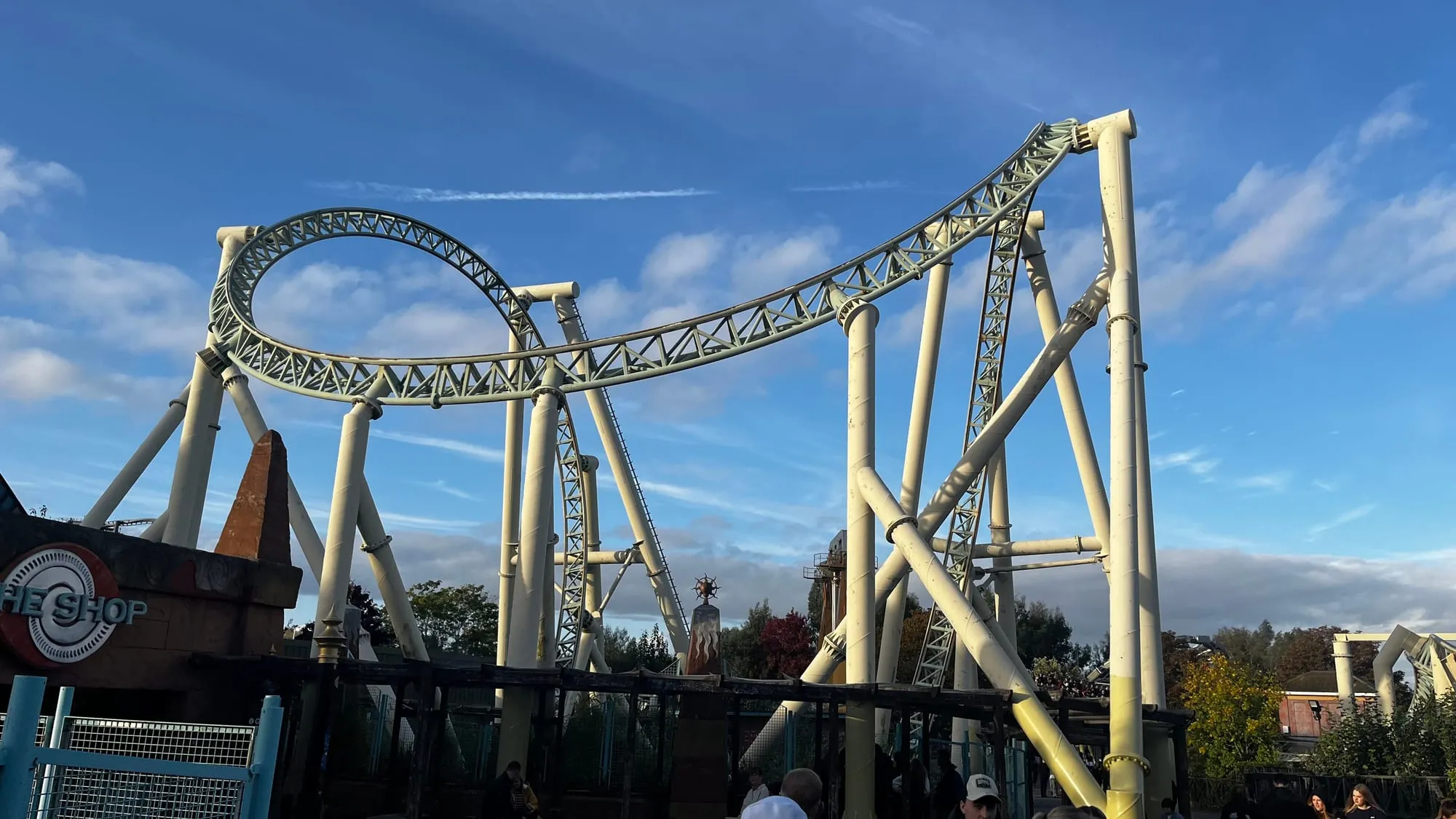 The cream track of Colossus at Thorpe Park twisting through its loops and rolls above the trees