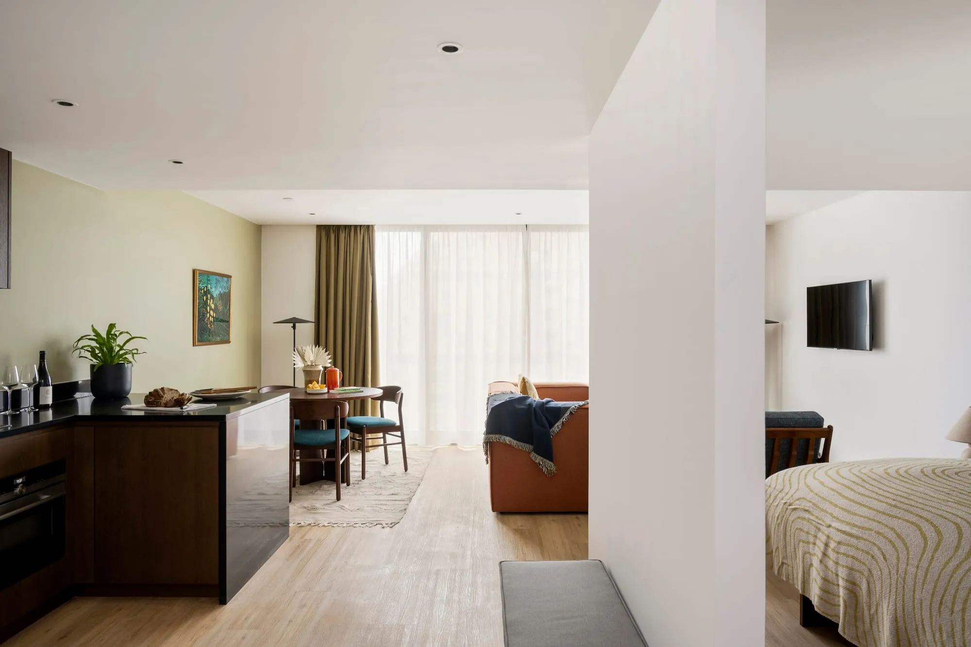 A studio at Cove Landmark Pinnacle, with a kitchenette counter in the foreground, a dining table and sofa, and the bed visible beyond through an open partition