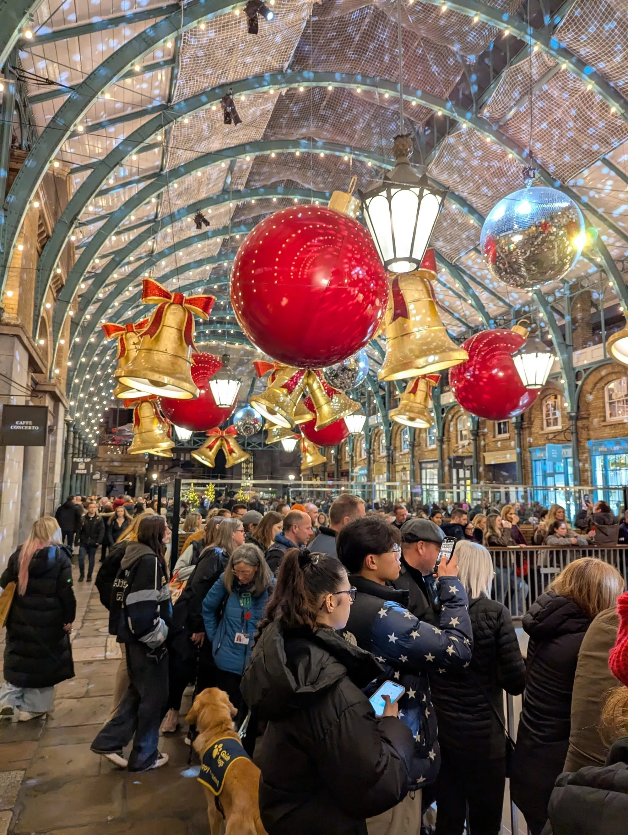 Giant illuminated red baubles and gold bells hanging from the Apple Market's cast-iron arcade at Covent Garden, with a disco ball among them