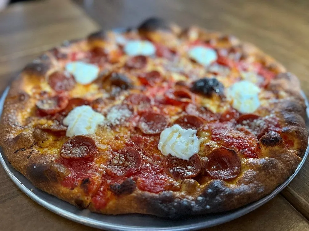 A New Haven-style pepperoni pizza at Crisp, its edge charred dark, topped with cupped pepperoni, tomato and spoonfuls of ricotta
