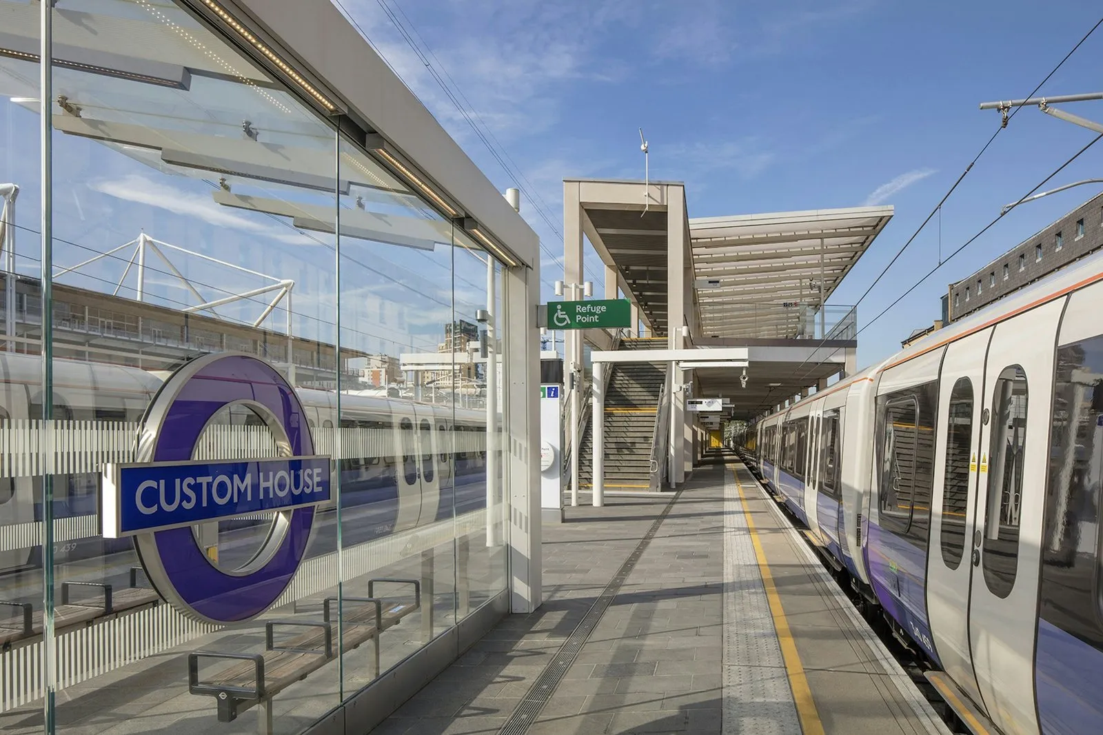 The purple Custom House roundel on the platform, with an Elizabeth line train alongside and the station canopy behind