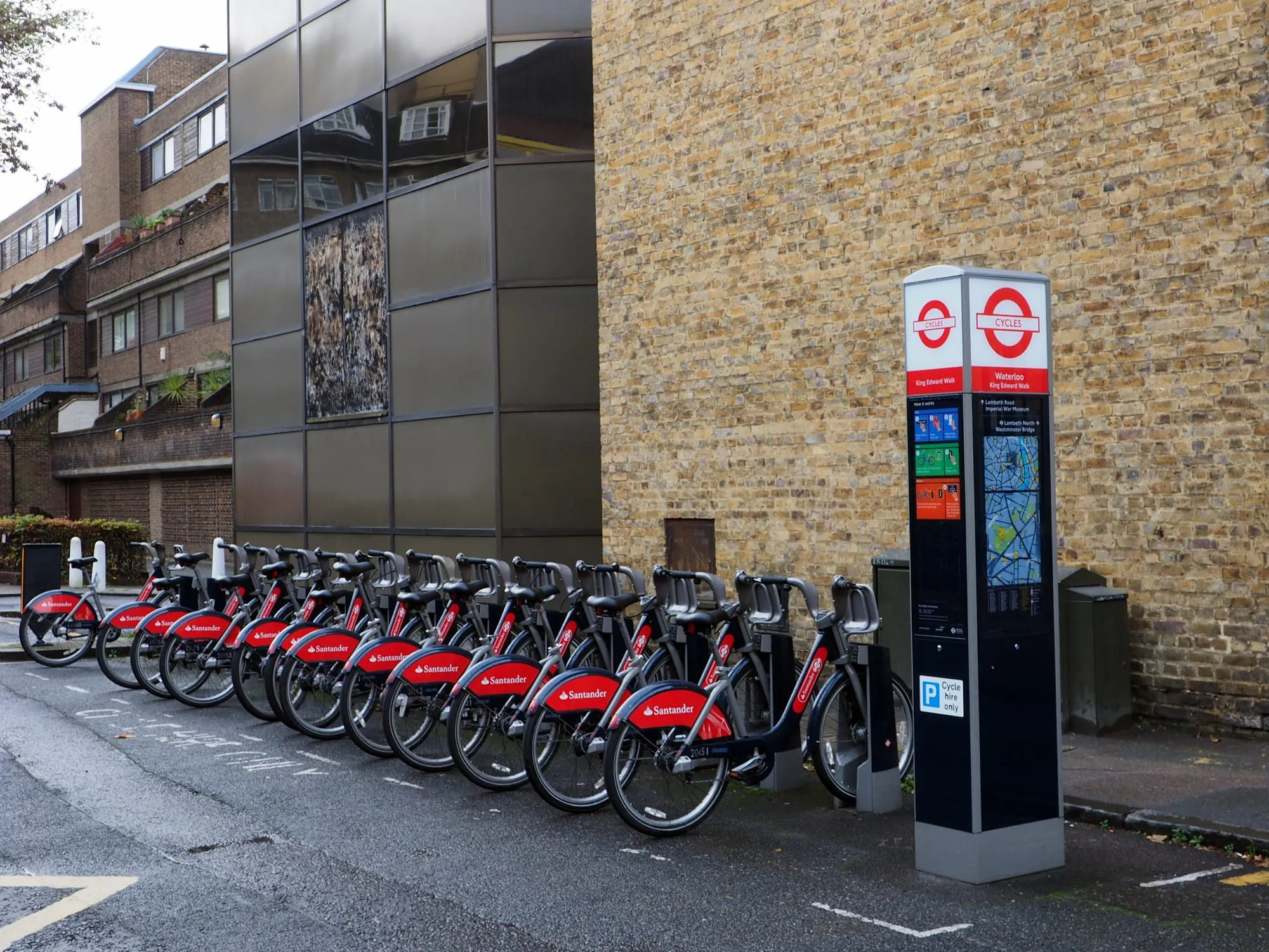 A row of red Santander Cycles hire bikes locked into a docking station on a London street