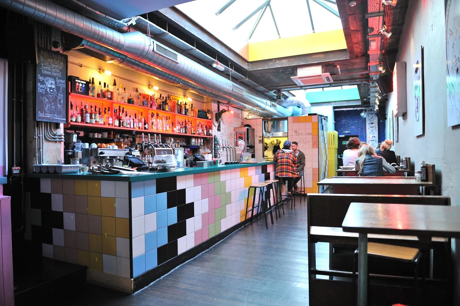 The tiled bar and wooden booths inside Dalston Superstore, under a skylight
