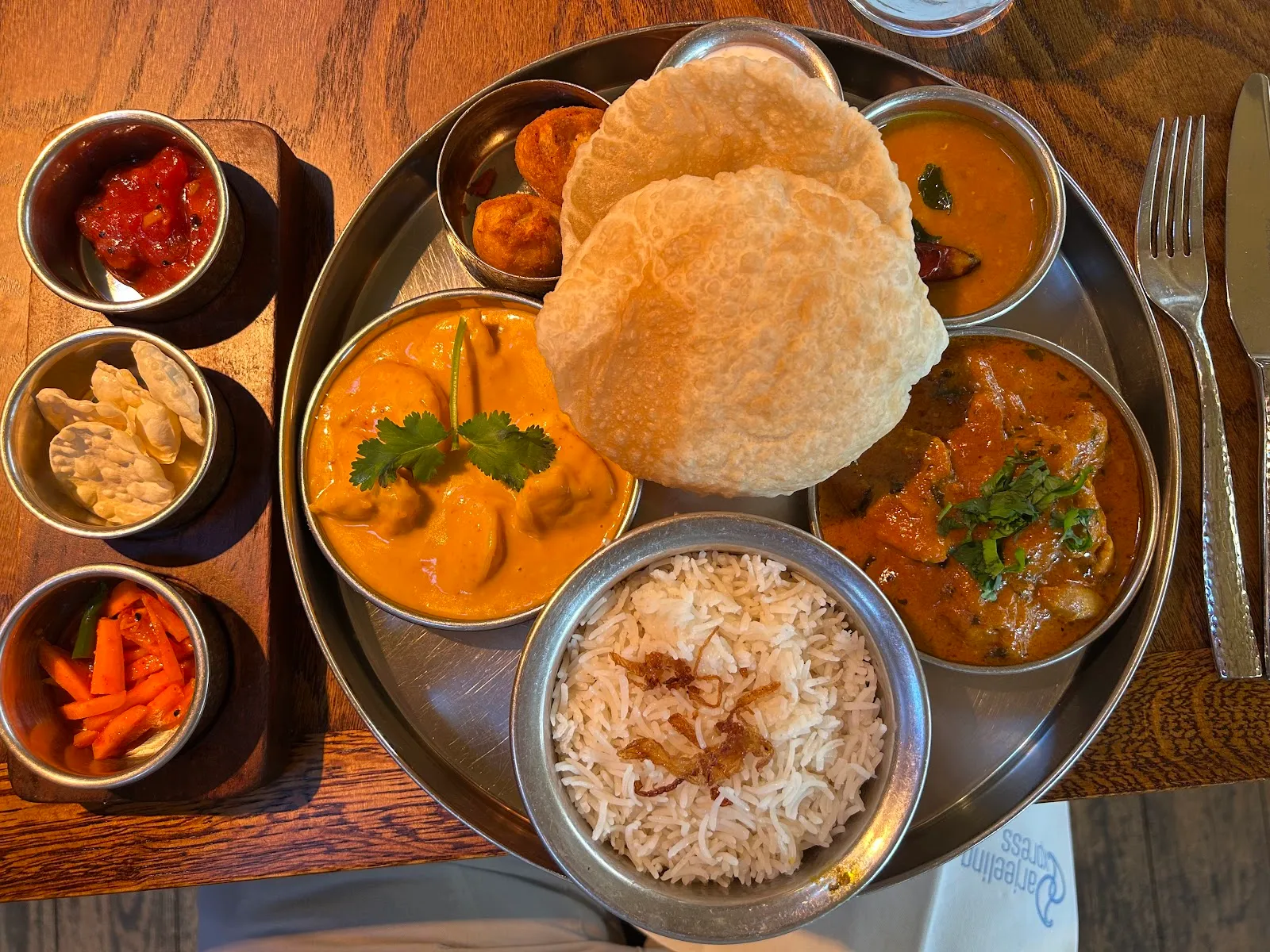 A royal thali at Darjeeling Express with puffed puris, curries, dal, steamed rice and chutneys beside an embroidered napkin