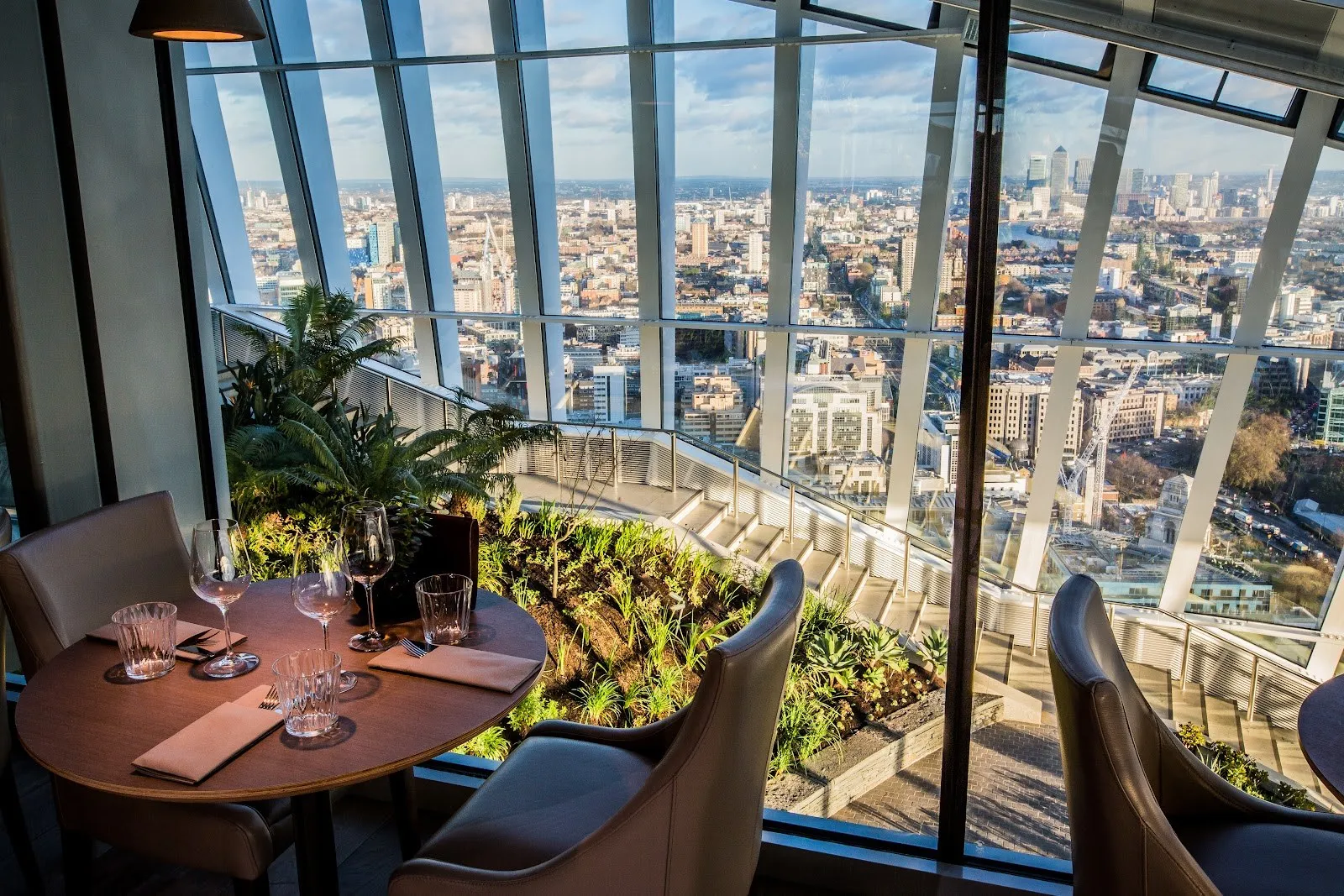 A round table set for two by the window, with planting on the terrace below and the City and Canary Wharf beyond